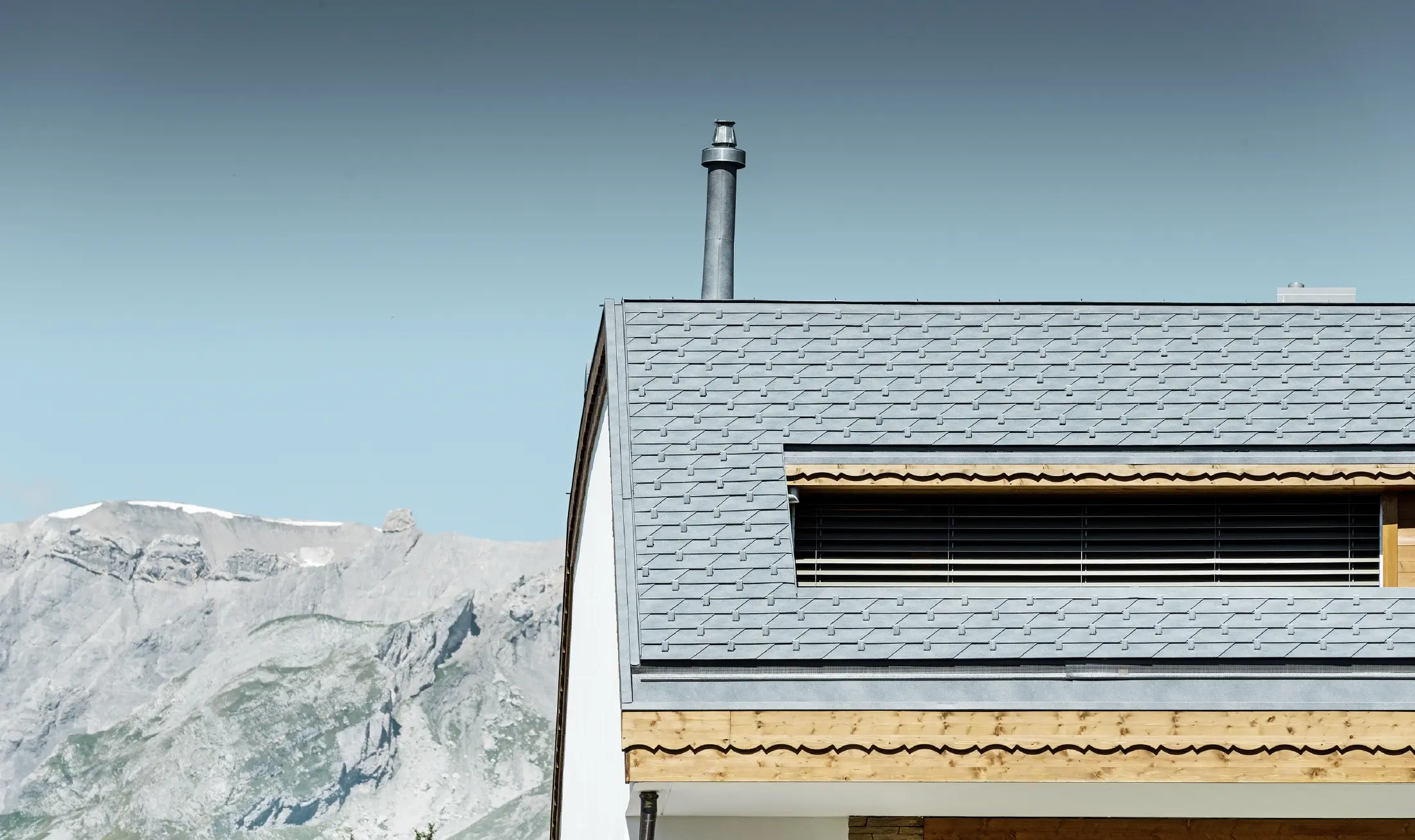 Meergezinswoning in Crans Montana (Zwitserland) met de bergen als decor, een gevel met speelse houten elementen en een dakbedekking bestaande uit aluminium PREFA-dakschindels in steengrijs