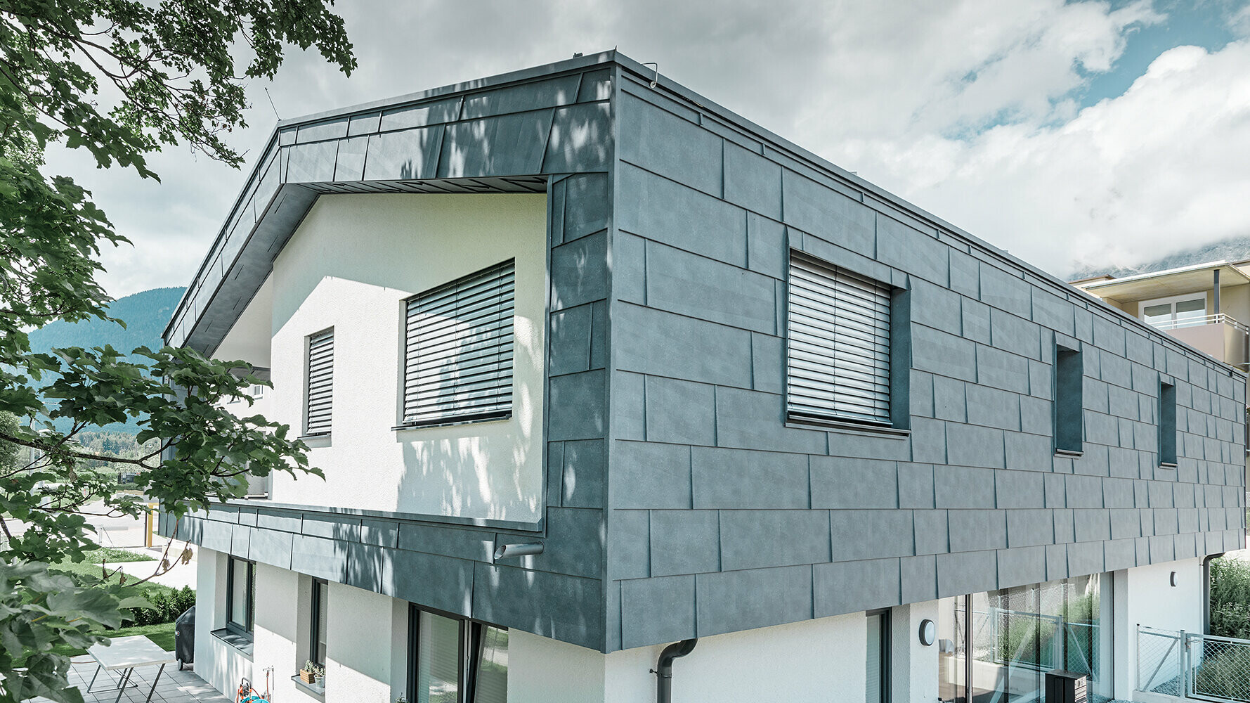 Maison individuelle revêtue de panneaux de façade FX.12 PREFA couleur gris pierre Maison individuelle moderne sans avancée de toit. L’étage supérieur a été recouvert de panneaux de façade FX.12 PREFA couleur gris pierre et le reste de la façade a été crépi en blanc.