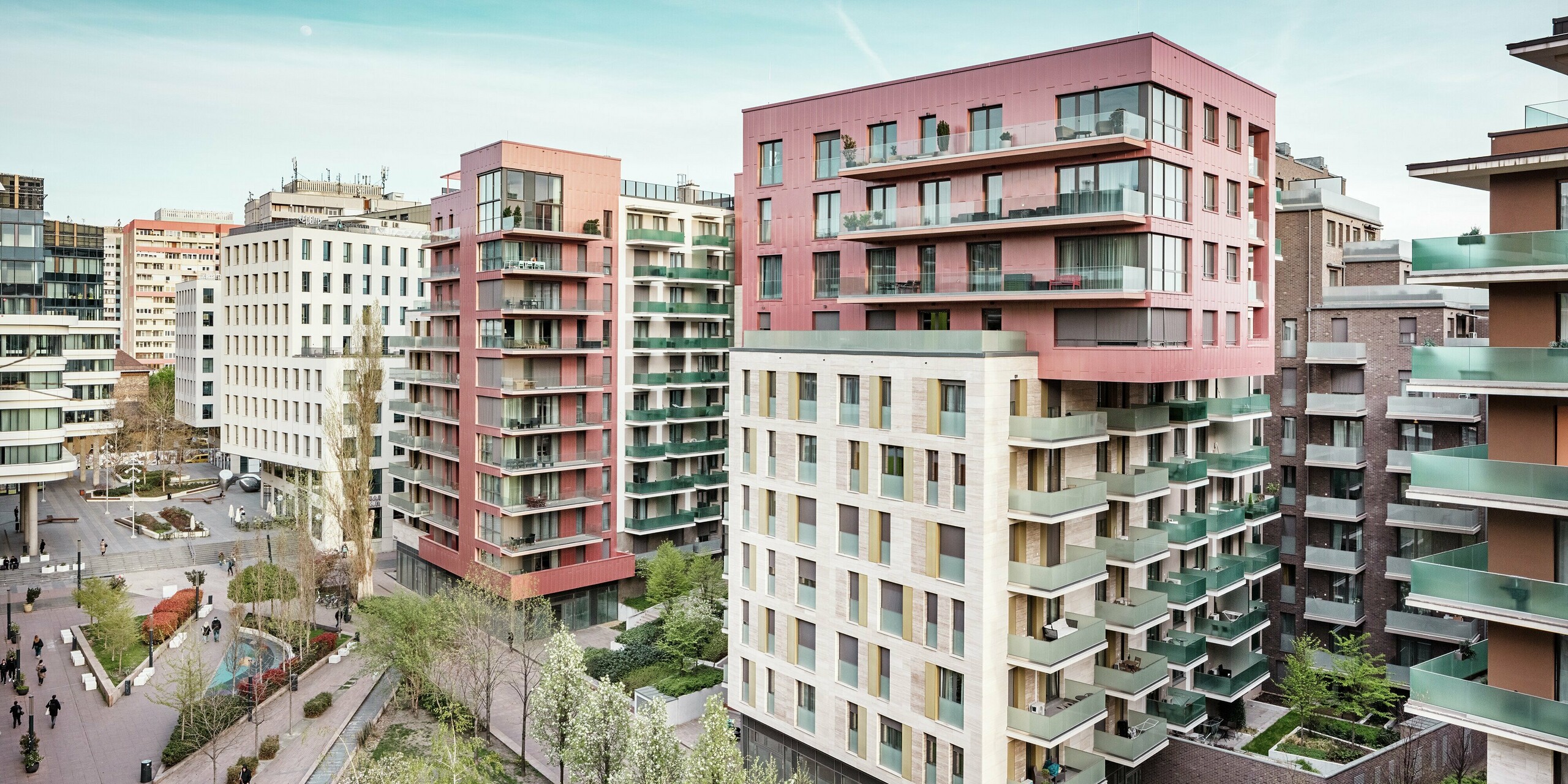 Vue d'ensemble saisissante du Grand Corvin Ensemble, dans le quartier Corvin de Budapest. Les étages supérieurs, remarquables, sont conçus avec des panneaux de façade Siding PREFA, posés verticalement et finis dans une couleur métallisé saumon spéciale. Associés à la pierre naturelle et à de généreuses surfaces vitrées, ils créent un paysage urbain moderne et de grande qualité. La façade en aluminium durable souligne la diversité architecturale et les aspirations durables de ce projet de rénovation urbaine globale.