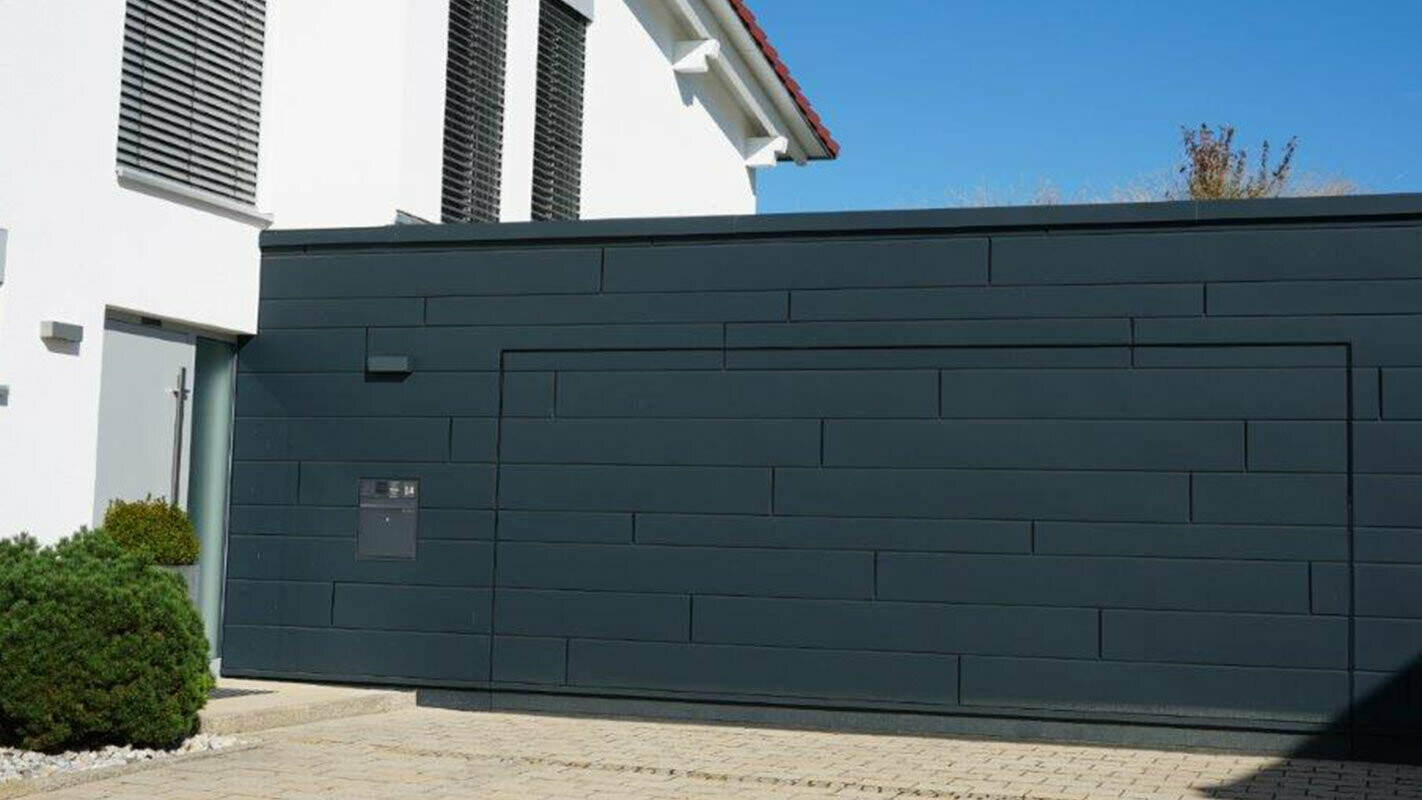 Fassade einer Garage nach der Sanierung mit PREFA Sidings in Anthrazit, Garagentor ist bündig mit der Fassade montiert