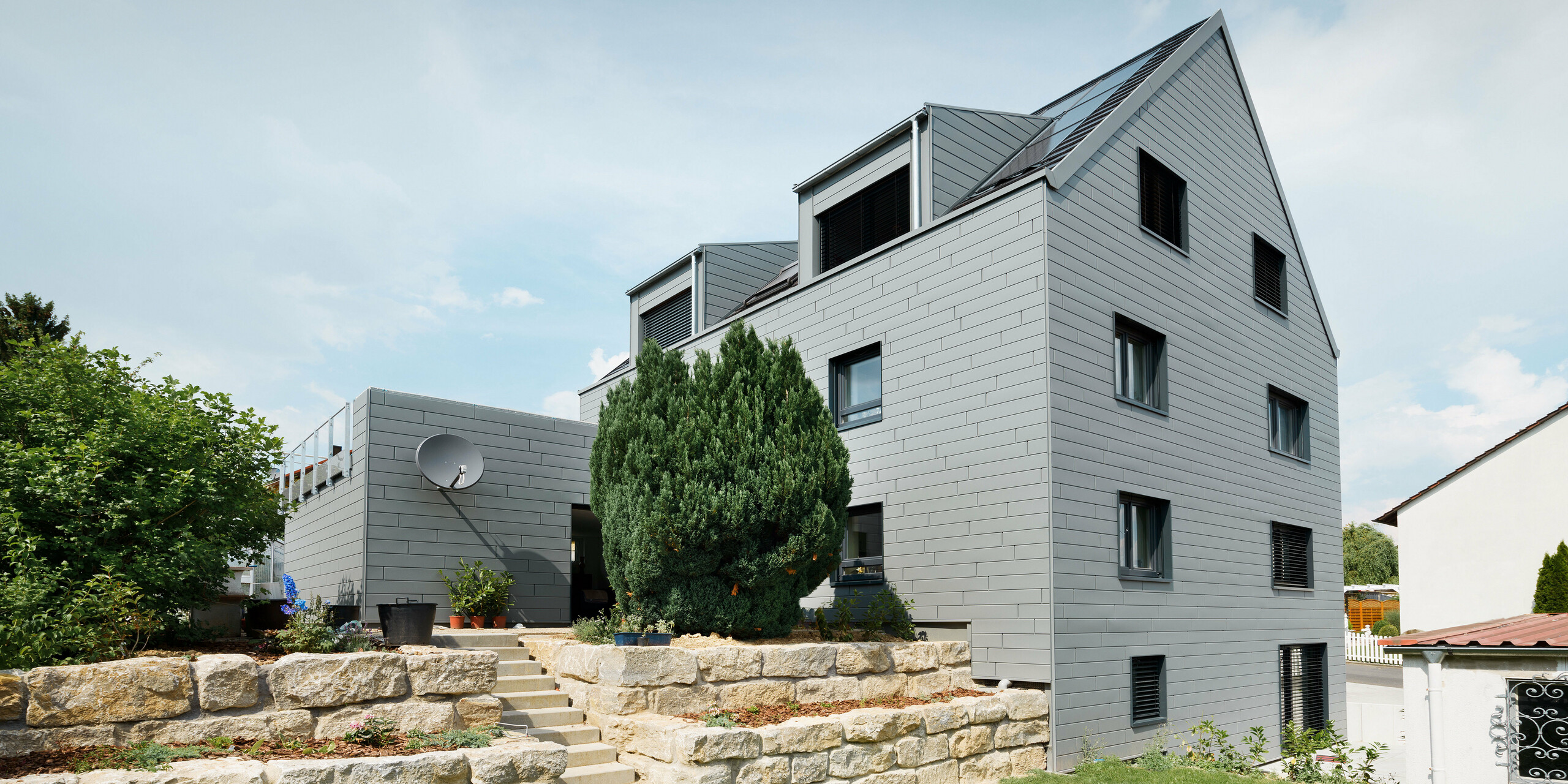 Die Gartenansicht des Hauses präsentiert die klaren, sauberen Linien der PREFA Sidings in der Farbe P.10 Hellgrau. Besonders hervorzuheben ist die geschmackvolle Steintreppe, die zur Terrasse führt und das Haus effektvoll in Szene setzt.