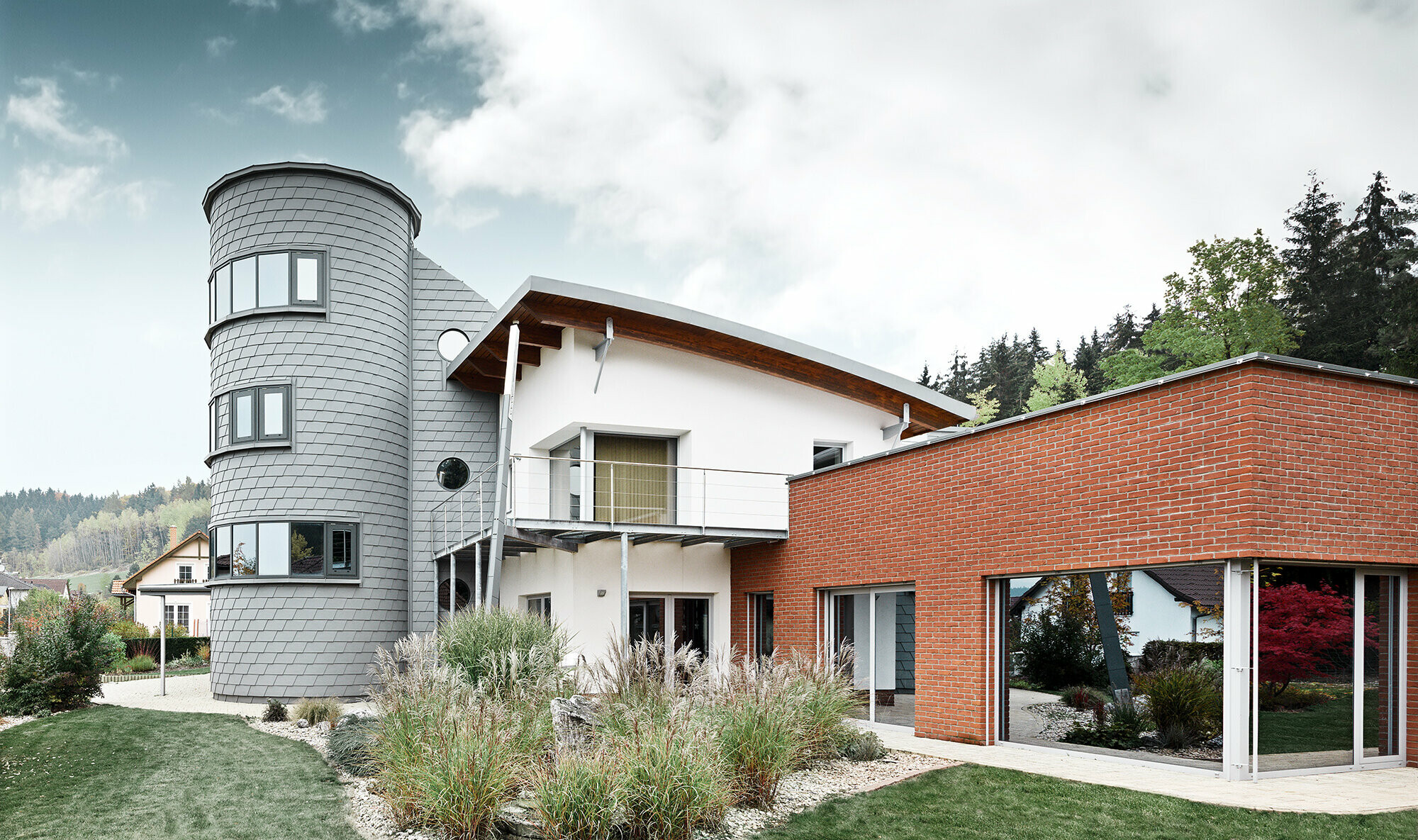 Einfamilienhaus mit Turmzubau, der runde Turm ist mit der PREFA Wandschindel in Patina Grau verkleidet 