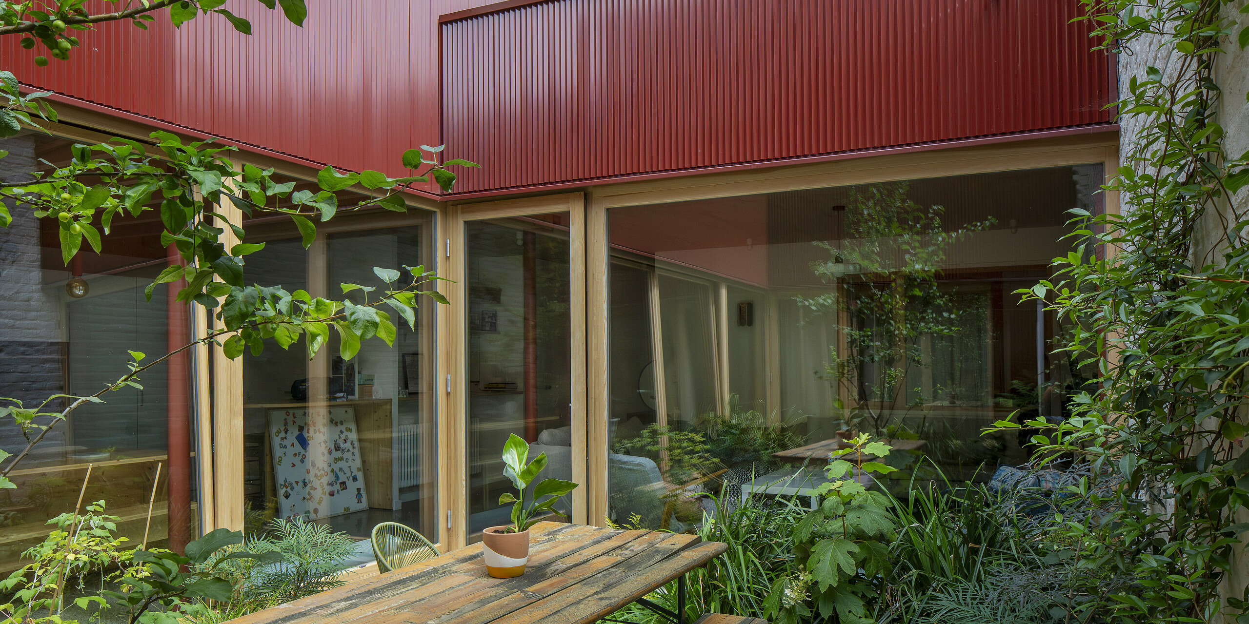 Einladender Rückzugsort in Lille: Das rote PREFA Zackenprofil verleiht der Fassade zum Innenhof eine dynamische, vertikale Struktur. Große Fenster öffnen den Raum ins Grüne und lassen Licht ins Innere strömen. Die Kombination aus Aluminium, Holz und Glas wirkt nicht nur hochwertig und modern, sondern ist auch extrem pflegeleicht.