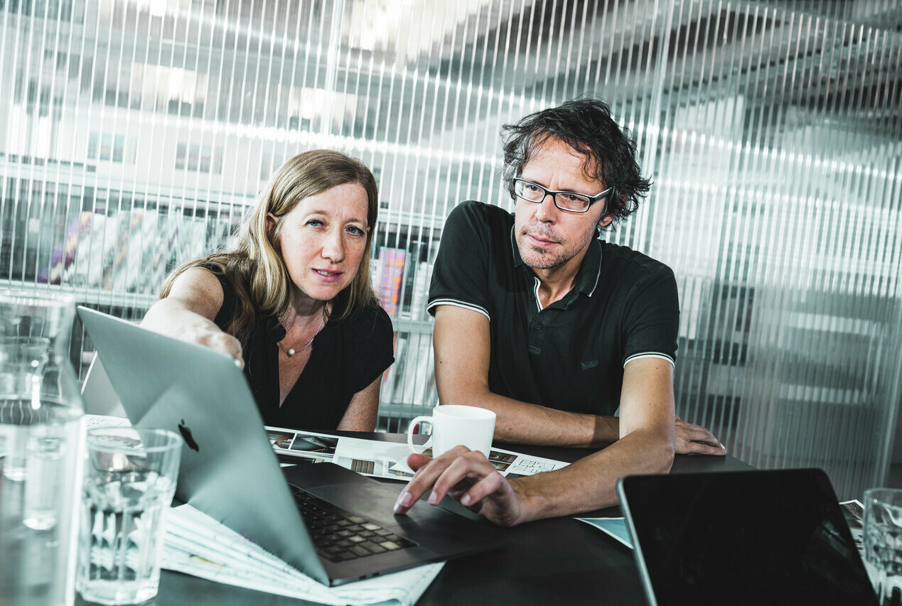 das federführende Architekten-Duo sitzen vor einem Laptop und planen das Bauvorhaben