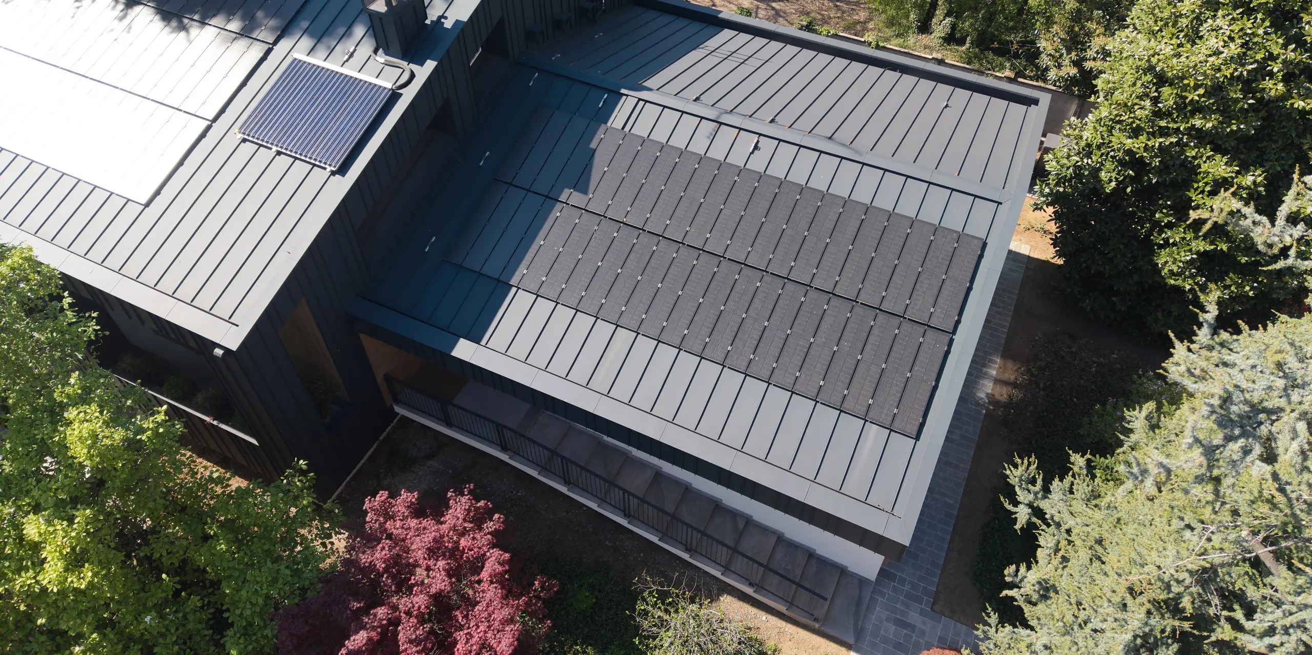 Luftaufnahme der Villa Castellanza mit PREFALZ Dach in P.10 Anthrazit und innovativen PREFALZ Solarmodulen. Die präzise gestaltete Aluminiumdachlandschaft überzeugt durch klare Linien und eine elegante Optik. Nachhaltige Energiegewinnung, hohe Witterungsbeständigkeit und die langlebige Qualität von PREFA verbinden Architektur, Funktion und Design auf beeindruckende Weise.