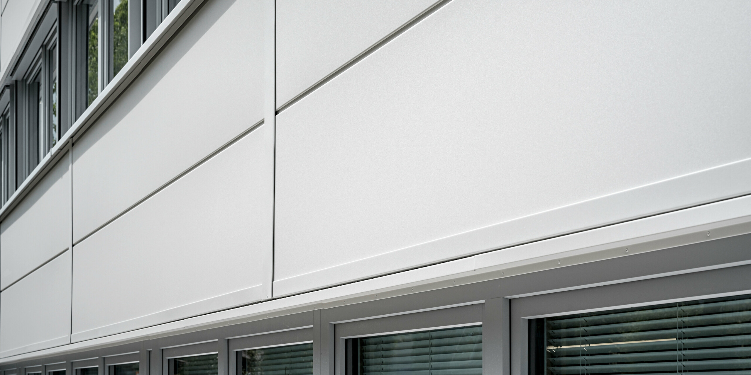 Des Sidings PREFA grand format entourent un bâtiment d'entreprise à Oberschleißheim (Allemagne). Les éléments de façade extra-larges en aluminium ont été choisis dans la couleur blanc Prefa.