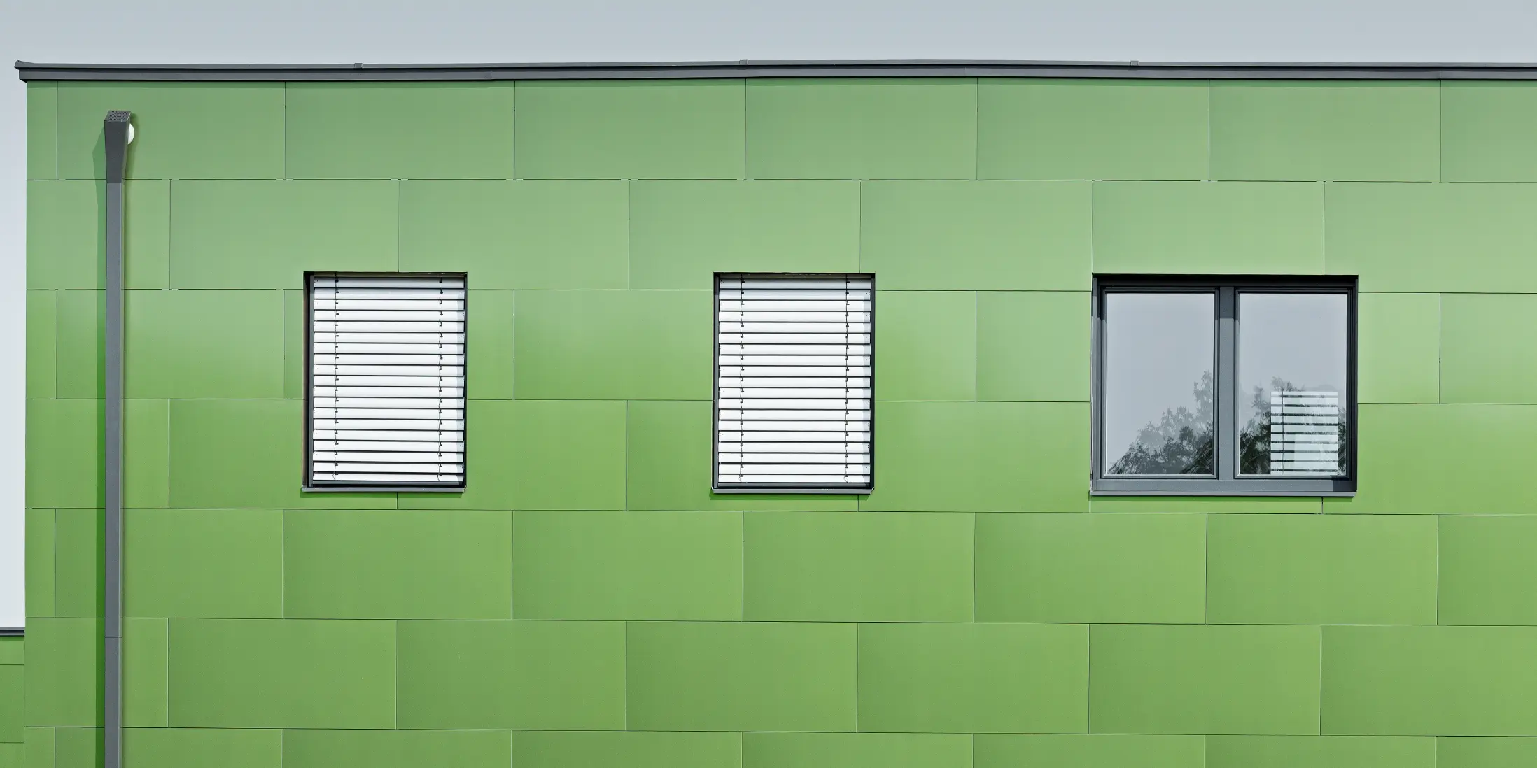 Frontalansicht der PREFA Aluminium Verbundplatte mit Chamäleon Optik und wechselnden Farben. Ganz links seht man das eckige Ablaufrohr, das PREFA Quadratrohr