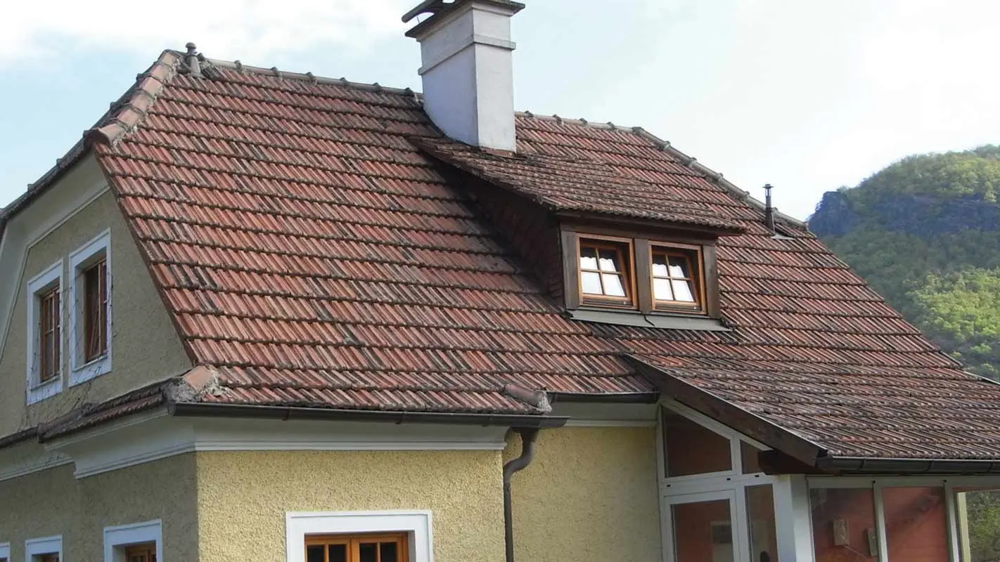 Altes Einfamilienhaus vor der Dachsanierung mit Ziegeldach und rauer, gelber Putzfassade