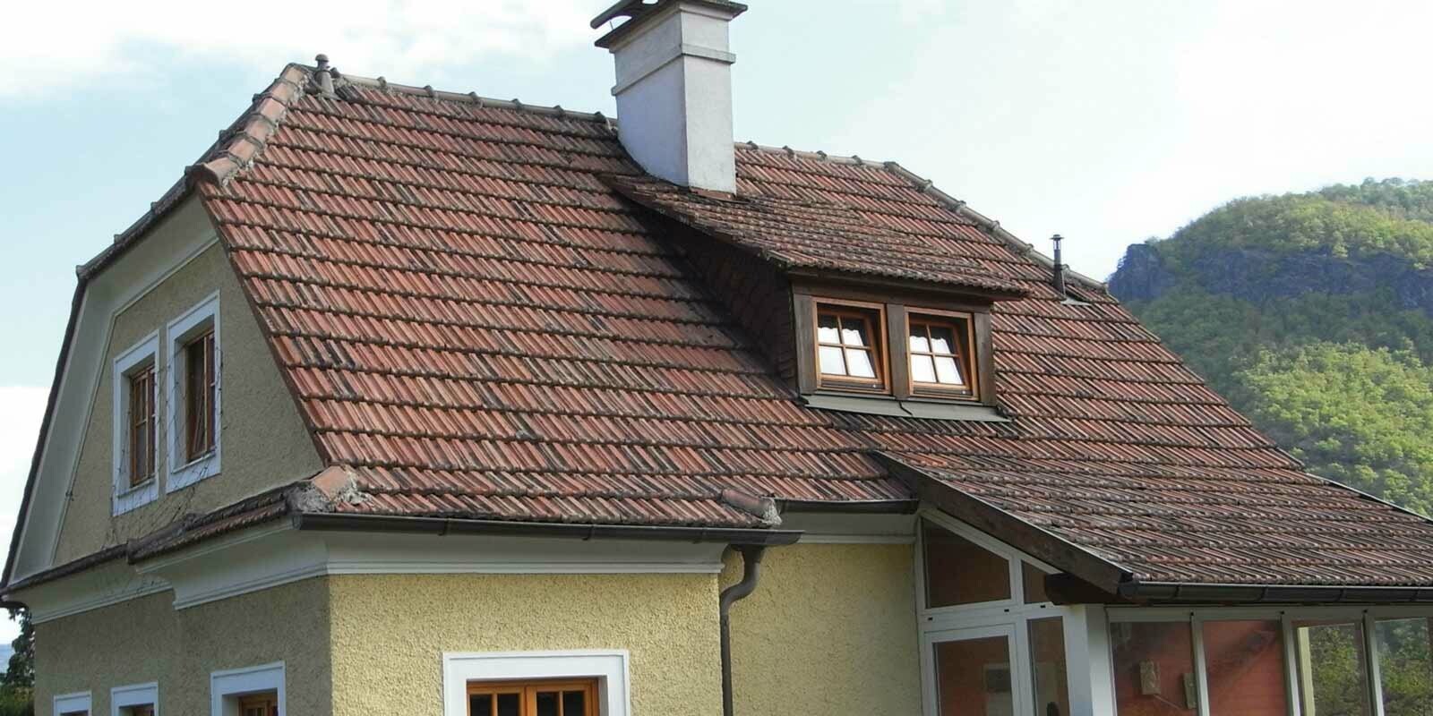 Ancienne maison individuelle avant la rénovation de toiture, avec toit en tuiles et façade brute en crépi, jaune