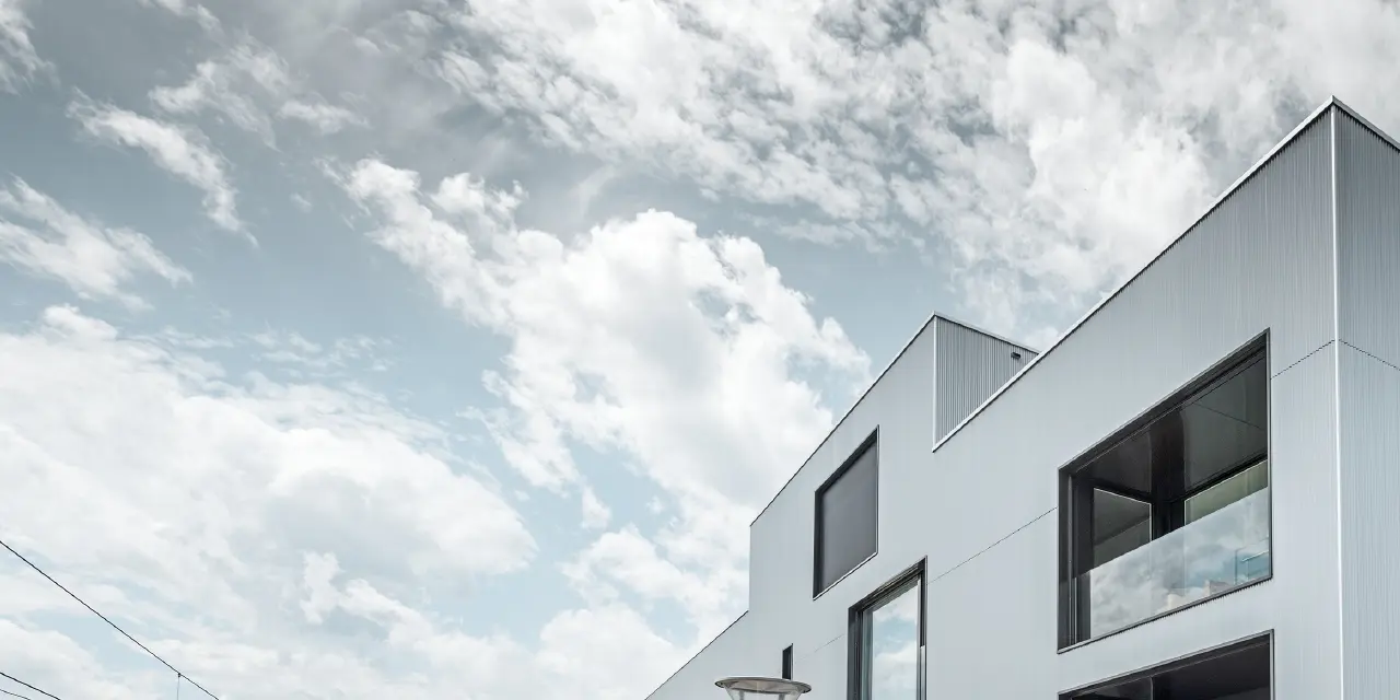 Bâtiment de société moderne à toit plat et façade alu ; pour la façade, le choix s’est porté sur le profil triangle PREFA anodisé naturel.