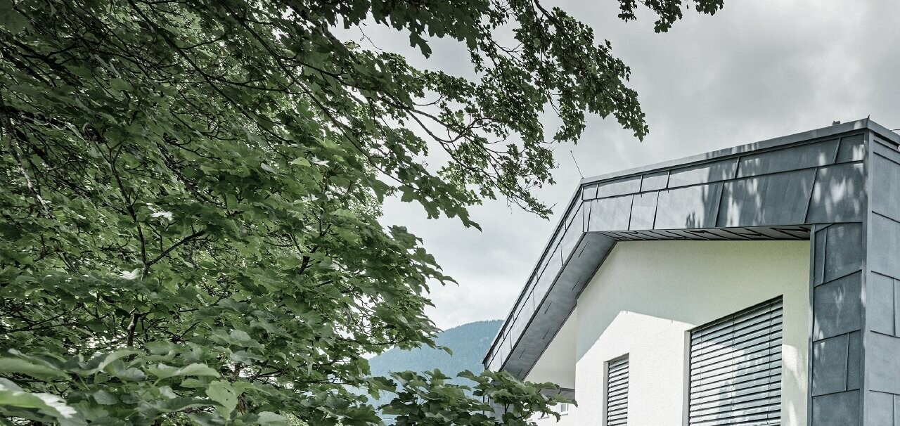 Structure moderne d’un bâtiment d’habitation avec toit à deux pans et sans avancée de toit ; l’habillage de façade a été réalisé avec le panneau de façade FX.12 PREFA couleur gris pierre.