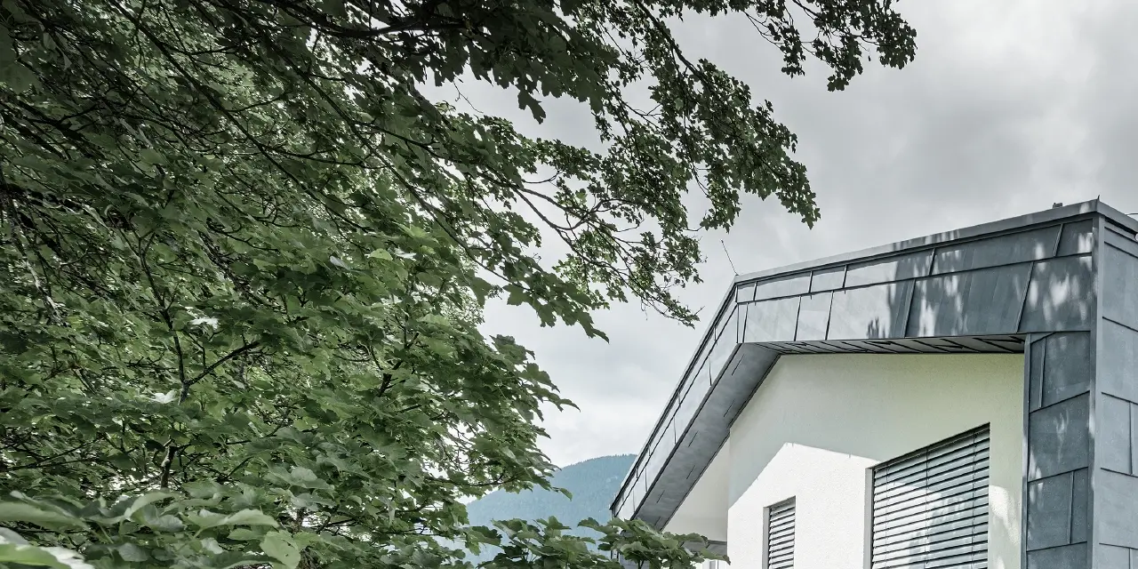 Structure moderne d’un bâtiment d’habitation avec toit à deux pans et sans avancée de toit ; l’habillage de façade a été réalisé avec le panneau de façade FX.12 PREFA couleur gris pierre.