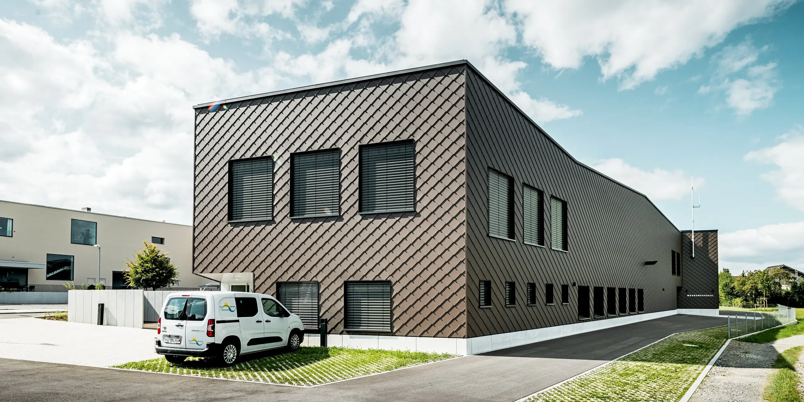 Anspruchsvolle Architektur in Wangen, Schweiz: Die großzügige Fassade des Infrastrukturgebäudes der Feuerwehr bzw. des Elektrizitätswerks ist vollständig mit PREFA Wandrauten in der Größe 29 × 29 und der Farbe P.10 Braun verkleidet. Die gleichmäßige Rautenstruktur umhüllt den gesamten Baukörper und verleiht ihm eine markante, moderne Ausstrahlung. Die langlebige Aluminiumfassade überzeugt durch hohe Witterungsbeständigkeit, geringen Wartungsaufwand und eine dauerhaft hochwertige Optik.