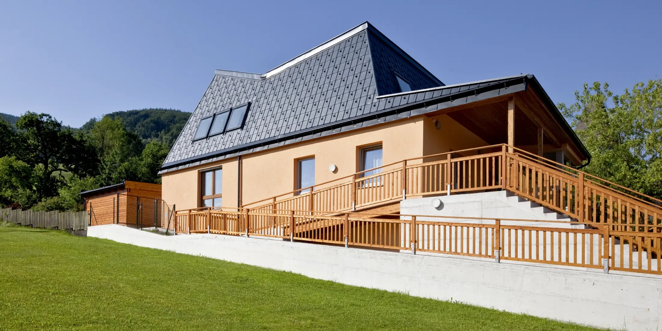 Kindergarten mit oranger Putzfassade und verwinkeltem Dach, gedeckt mit der PREFA Dachplatte in P.10 Anthrazit;