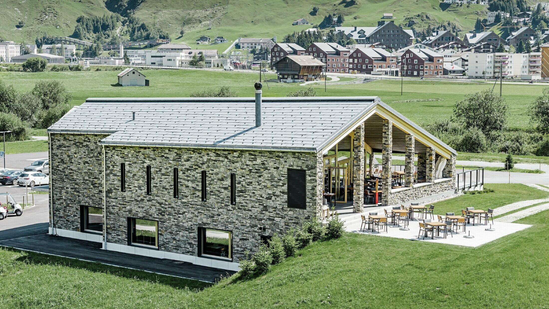 Modern clubhuis van golfterrein in Andermatt (Zwitserland) met gevel in natuursteen en aluminium FX.12 dakpanelen in steengrijs van PREFA 