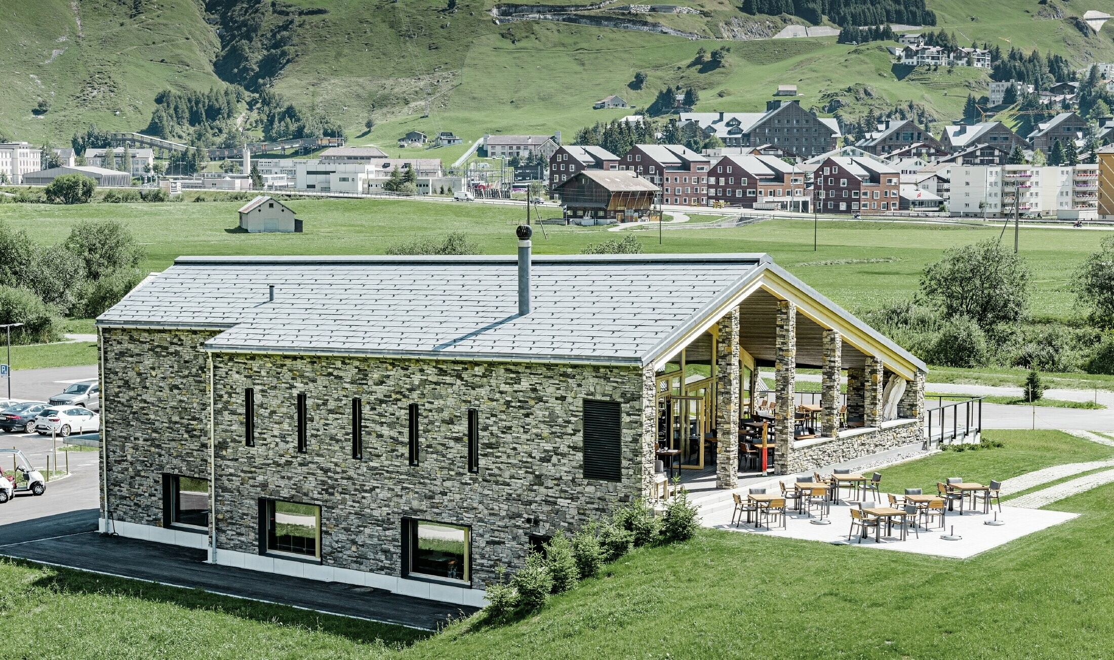 Club-house moderne du parcours de golf d’Andermatt en Suisse — Façade en pierre et panneaux de toiture FX.12 PREFA en aluminium de couleur gris pierre