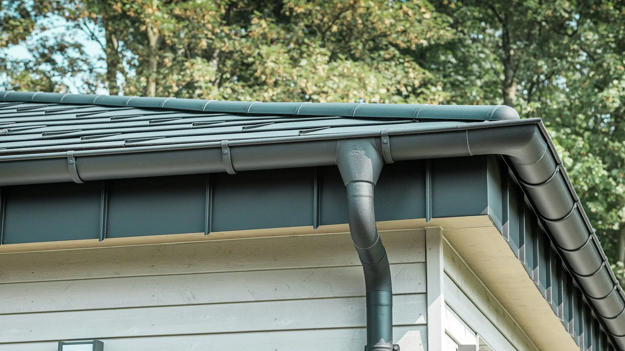 Detailaanzicht van het PREFA dakafvoersysteem van een bungalow in Rommerskirchen. De hoogwaardige ardense goot en de afvoerbuis in P.10 zwart zorgen voor een veilige afvoer van het regenwater. De duurzame PREFA aluminiumproducten combineren functionaliteit met een modern, elegant design.