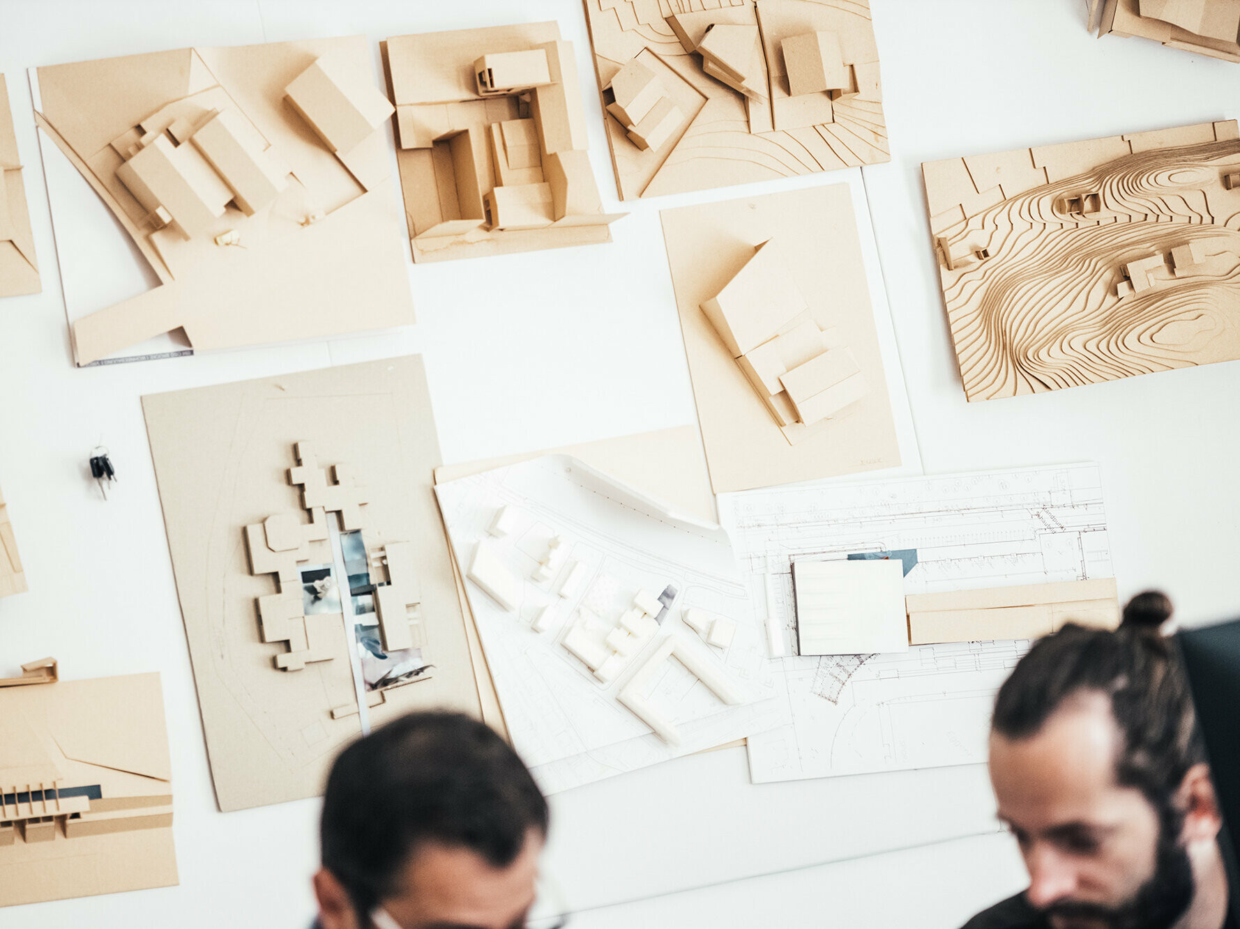 Aufnahme von Architekturmodellen an der Wand. Unscharf im Vordergrund: zwei Mitarbeiter des Büros.