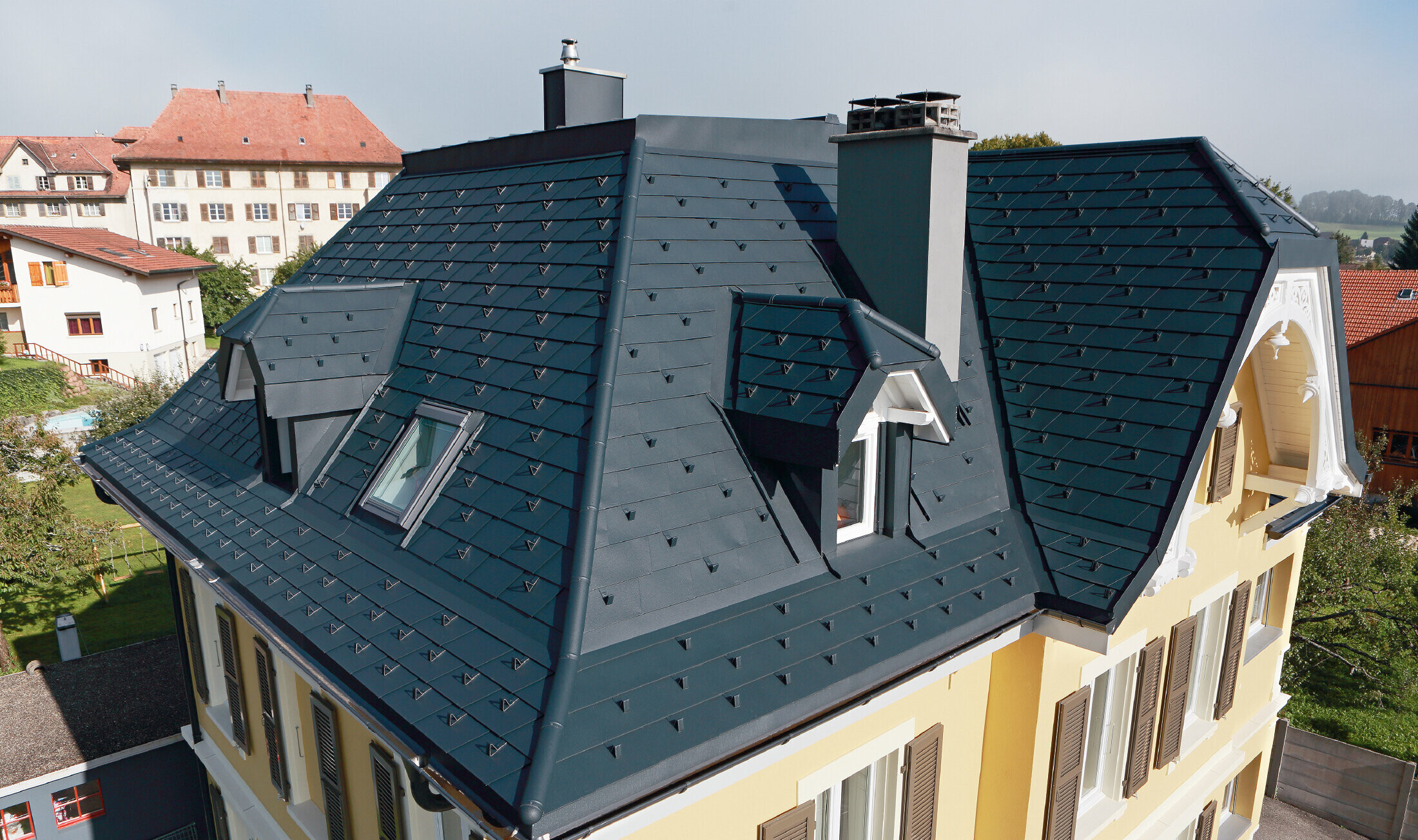 Villa in Zwitserland, het dak heeft veel kielgoten en kleine dakkapellen, het is bekleed met aluminium schindels van PREFA in P.10 antraciet