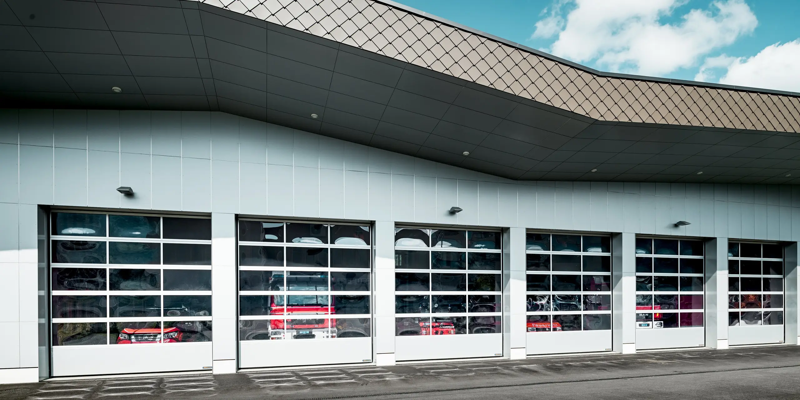 Moderne Fahrzeughalle der Feuerwehr Wangen mit großzügiger Fassade aus Aluminium Verbundplatten in P.10 Prefaweiß und markantem Dachrand aus PREFA Wandrauten 29 × 29 in P.10 Braun. Die dynamische Linienführung und die charakteristische Rautenstruktur verleihen dem Gebäude eine kraftvolle Architektur. PREFA Aluminium überzeugt durch Langlebigkeit, hohe Witterungsbeständigkeit und dauerhaft hochwertige Optik.