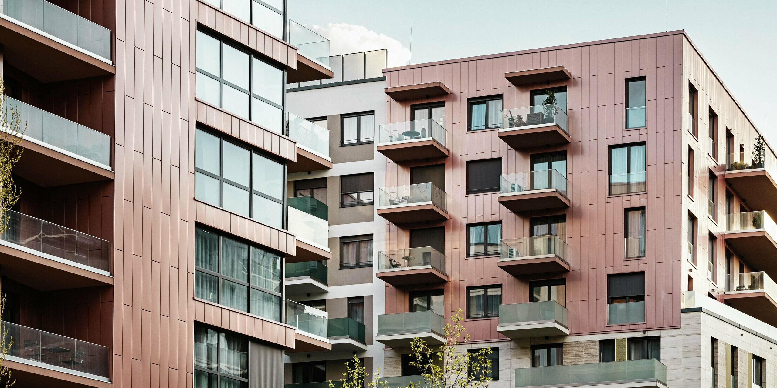 Détail de la façade du complexe résidentiel Grand Corvin, dans le quartier revitalisé de Corvin à Budapest. Les panneaux de façade Siding PREFA, posés verticalement et déclinés dans une couleur saumon métallisée, soulignent l'aspect moderne des étages supérieurs du bâtiment. Associé à de grandes façades vitrées et à de la pierre naturelle, le revêtement en aluminium durable crée un paysage urbain harmonieux et de grande qualité.