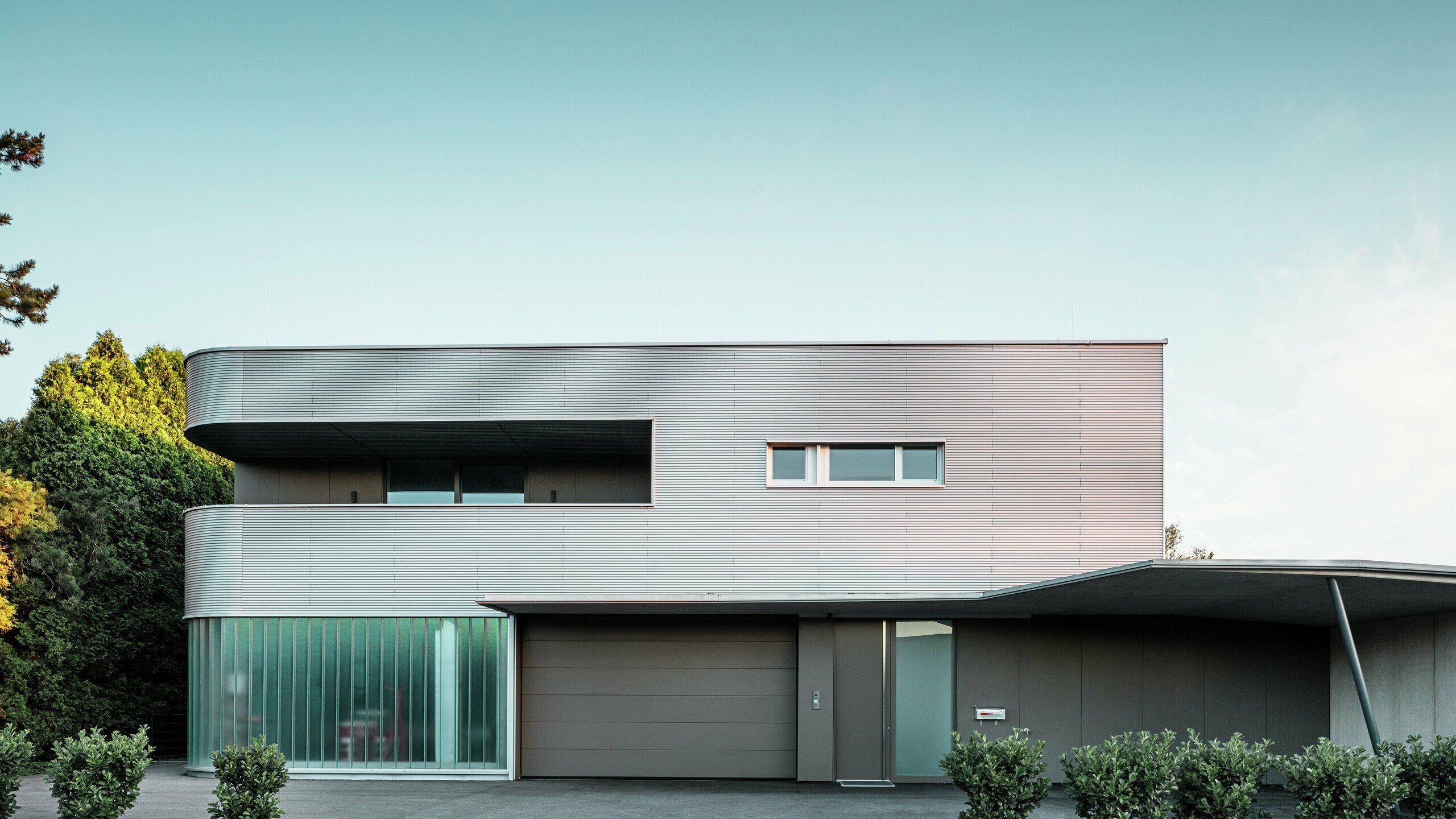 Modernes Wohnhaus mit naturblanker Fassade aus der PREFA Profilwelle mit Garage bei Tageslicht.