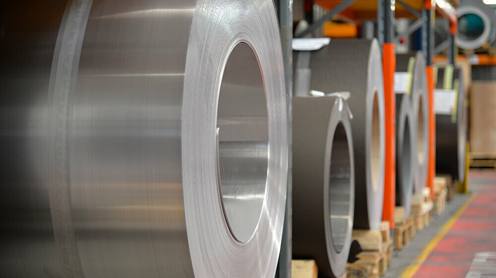 Bobines d’aluminium ("coils") sur palettes en bois : au premier plan, un rouleau en aluminium naturel et derrière, d’autres bandes et feuilles d’aluminium.
