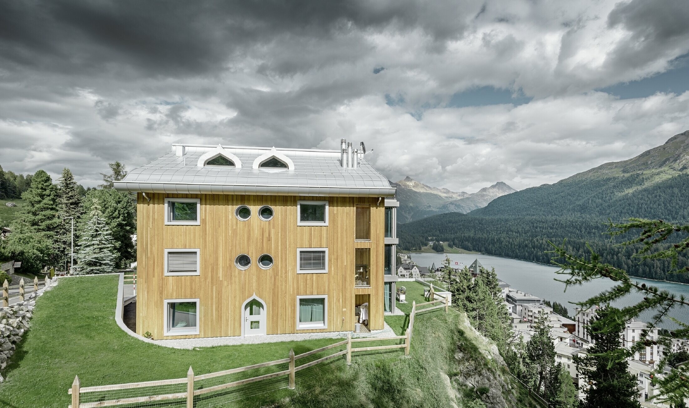 Wohnhausanlage in St. Moritz mit Holzfassade und Aluminiumdach mit geschwungener Traufe in silbermetallic