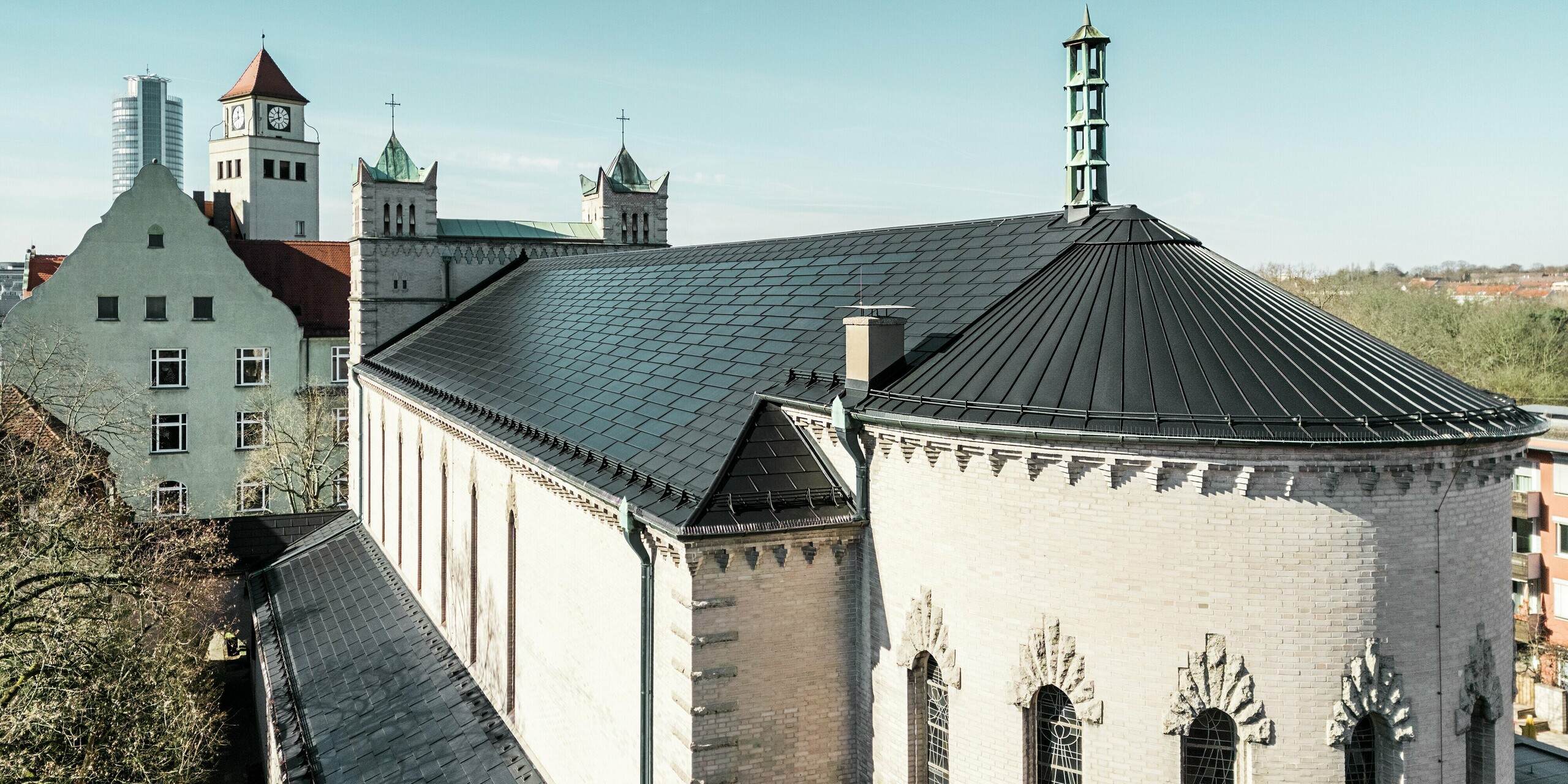 La rénovation de l'église Saint-Charles-Borromée de Nuremberg illustre de manière impressionnante l'intégration harmonieuse de tuiles solaires PREFA modernes dans un bâtiment classé. Sur le toit, les tuiles solaires noires permettent une production d'électricité efficace et respectueuse de l'environnement. Les dépendances de l'église ont été recouvertes de R.16 PREFA. L'imposante courbure à l'arrière du bâtiment a été recouverte d'une toiture à joint debout en aluminium.