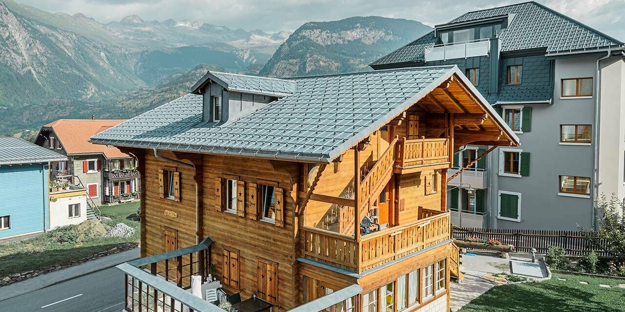 Traditioneel Zwitsers houten chalet met dakkapel en zadeldak; het dak is gedekt met de klassieke PREFA dakpannen in steengrijs.
