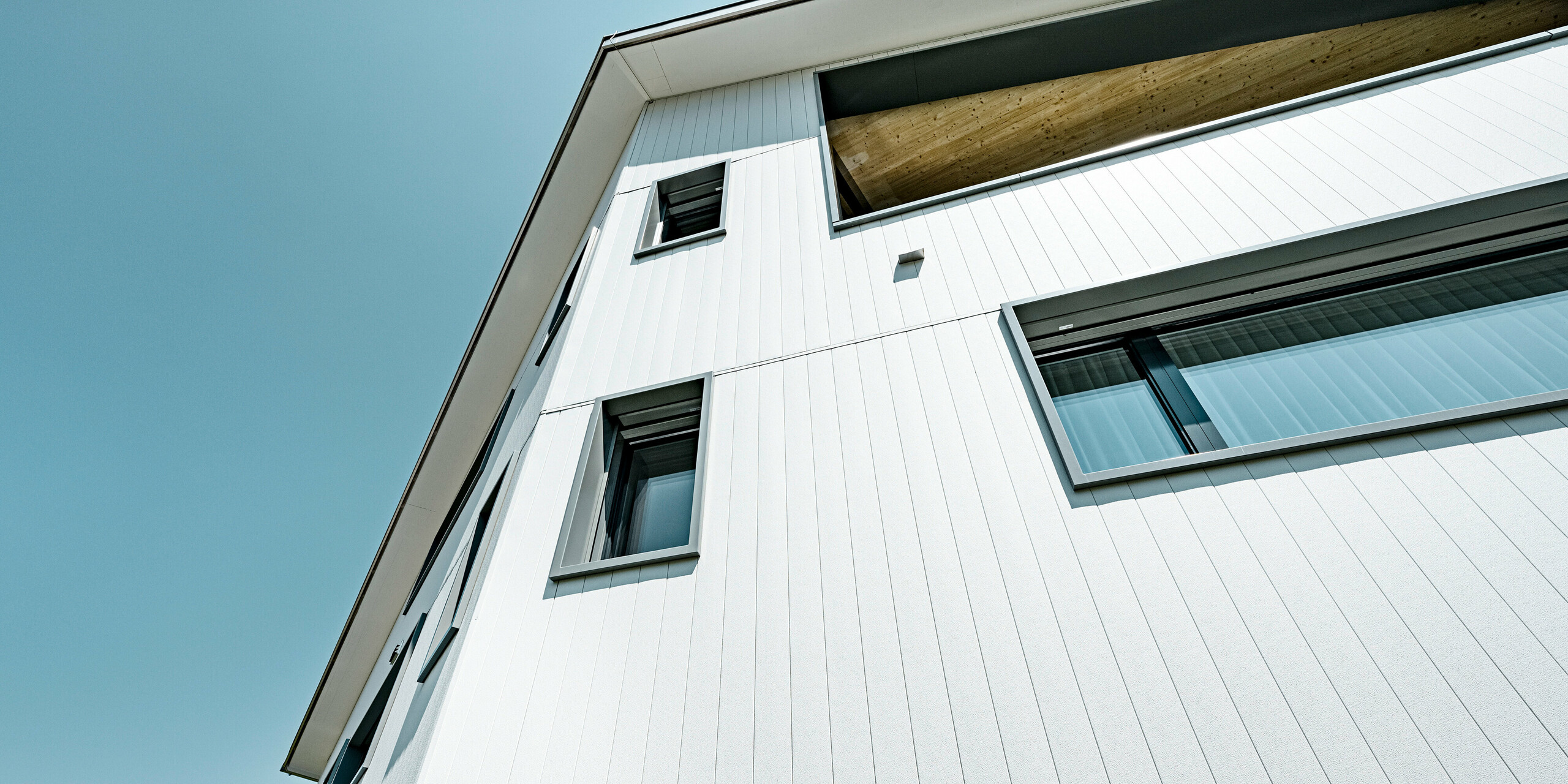 Detailansicht einer PREFA Aluminiumfassade in P.10 Prefaweiß, die ein Mehrfamilienhaus in Weissbad, Schweiz, verkleidet. Die Fassade zeigt die vertikale Montage der PREFA Sidings, welche die klaren Linien und die moderne Architektur des Gebäudes betonen. Das hochqualitative Material und das sorgfältige Design der Sidings reflektieren die Beständigkeit und das zeitgemäße Design, das PREFA für moderne Wohnkonstruktionen bietet.