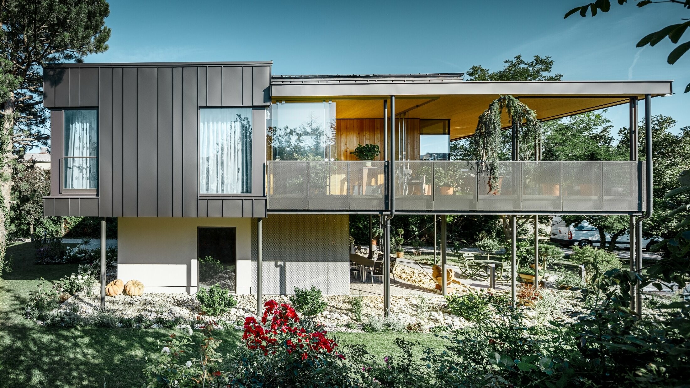 modernes Einfamilienhaus, ähnlich einem Baumhaus umgeben von einem großen Garten mit vielen Bäumen mit einer dezenten Winkelstehfalzfassade in schwarzgrau von PREFA