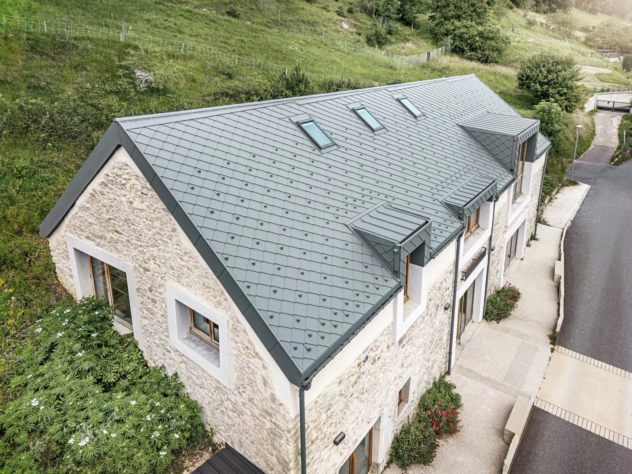 Blick auf das Dach der restaurierten Scheune „La Grange à Gaby“ in Engins, Frankreich. Das moderne PREFA-Aluminiumdach mit 29 × 29 cm großen Rauten fügt sich harmonisch in das historische Steingebäude ein und bietet langfristigen Schutz vor Witterungseinflüssen.