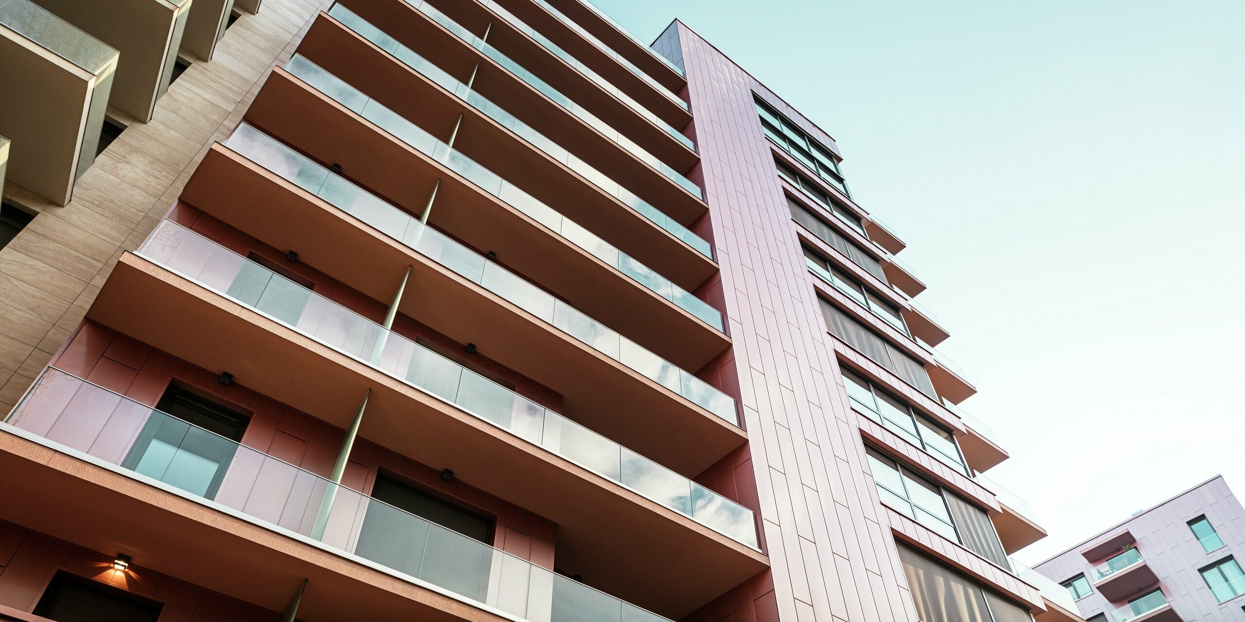 Vue dynamique de la façade en aluminium du complexe résidentiel Grand Corvin, dans le quartier de Corvin à Budapest. La structure verticale du bardage PREFA, couleur saumon métallisé, souligne l'aspect moderne du bâtiment. Les panneaux de façade durables et résistants aux intempéries soulignent l'architecture de haute qualité et ajoutent une touche d'élégance à l'environnement urbain.