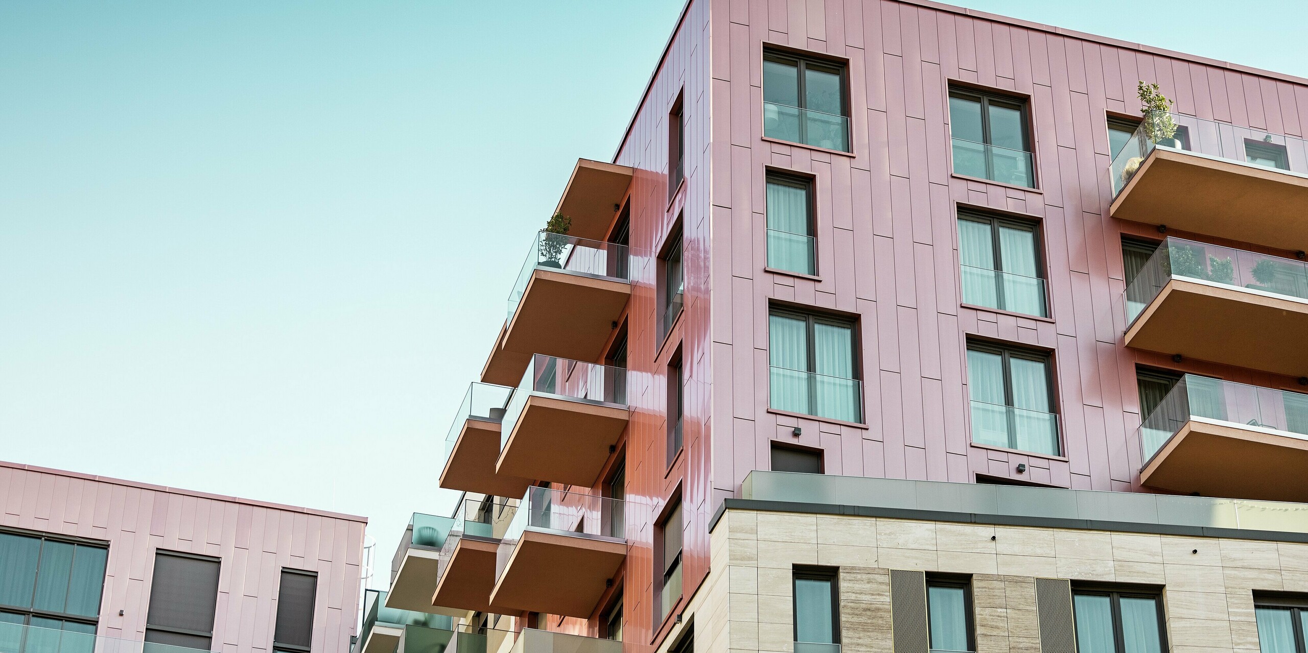 Un immeuble résidentiel moderne du quartier Corvin de Budapest arbore une façade PREFA remarquable, posée verticalement et dotée d'une finition saumon métallisé brossé. Les panneaux de façade en aluminium, posés avec précision, soulignent les lignes épurées du bâtiment et lui confèrent un aspect urbain de grande qualité. La façade PREFA, durable, incarne l'architecture moderne, la résistance aux intempéries et un mode de vie urbain sans entretien.