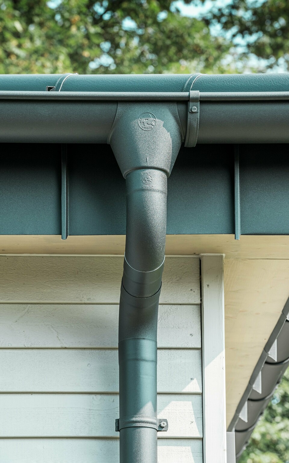 Nahaufnahme der robusten PREFA Dachentwässerung eines Bungalows in Rommerskirchen. Die hochwertige Saumrinne und das Ablaufrohr in P.10 Schwarz bieten optimalen Schutz vor Witterungseinflüssen. Langlebigkeit und Funktionalität verbinden sich hier mit elegantem Design aus Aluminium.