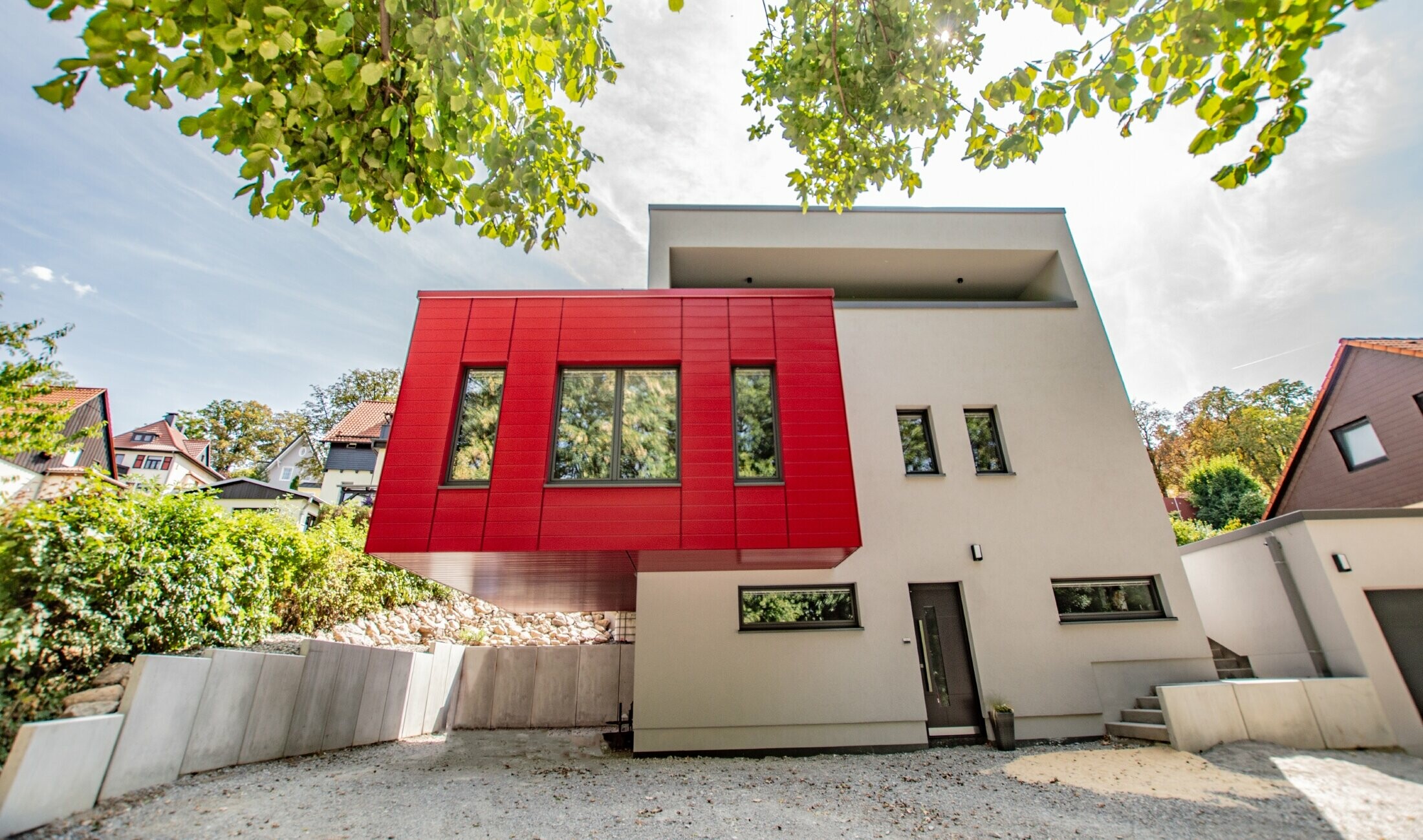 Auskragender Gebäudeteil mit den PREFA Sidings in Rubinrot verkleidet. Großer roter Erker, der sich von der weißen Fassade abhebt.