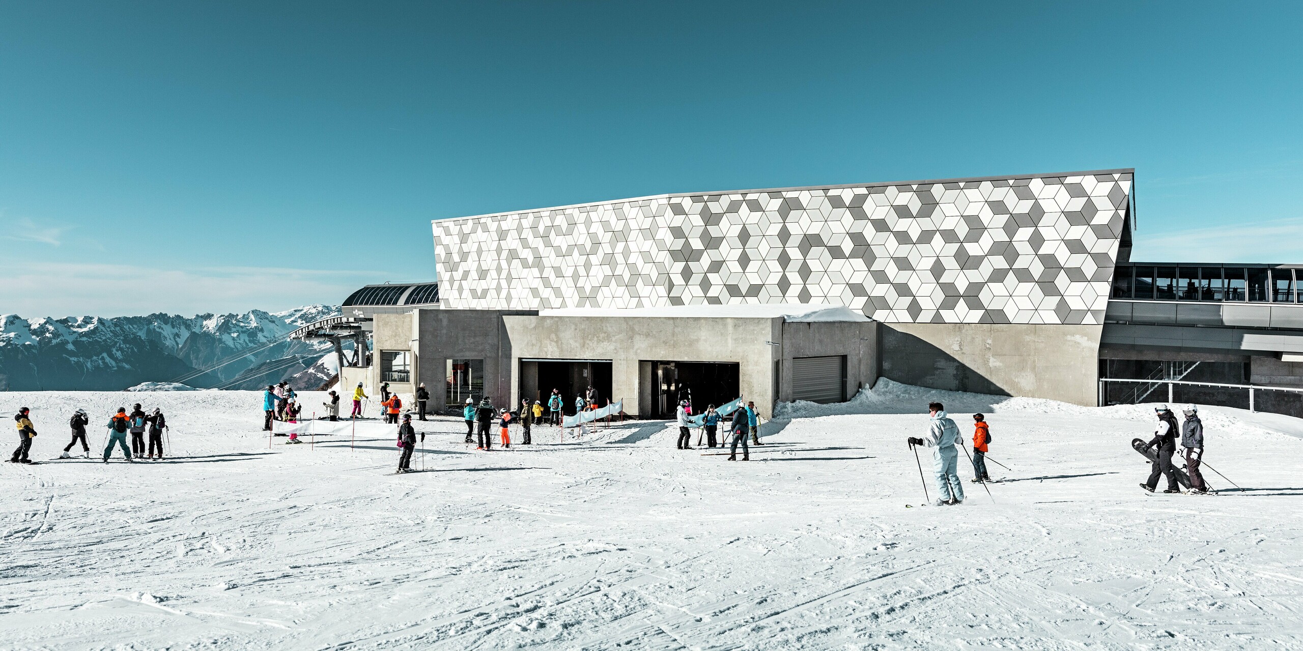 La station intermédiaire du téléphérique 3S des Deux Alpes se distingue par sa façade moderne. L'impressionnante enveloppe du bâtiment a été conçue avec des panneaux composites en aluminium PREFABOND, ornés d'un motif en losanges saisissant. L'association de différentes nuances de blanc et de gris s'harmonise parfaitement avec le paysage enneigé. La partie inférieure du bâtiment est en béton apparent. Ces matériaux robustes et résistants aux intempéries sont non seulement esthétiques, mais offrent également une protection durable contre les intempéries.