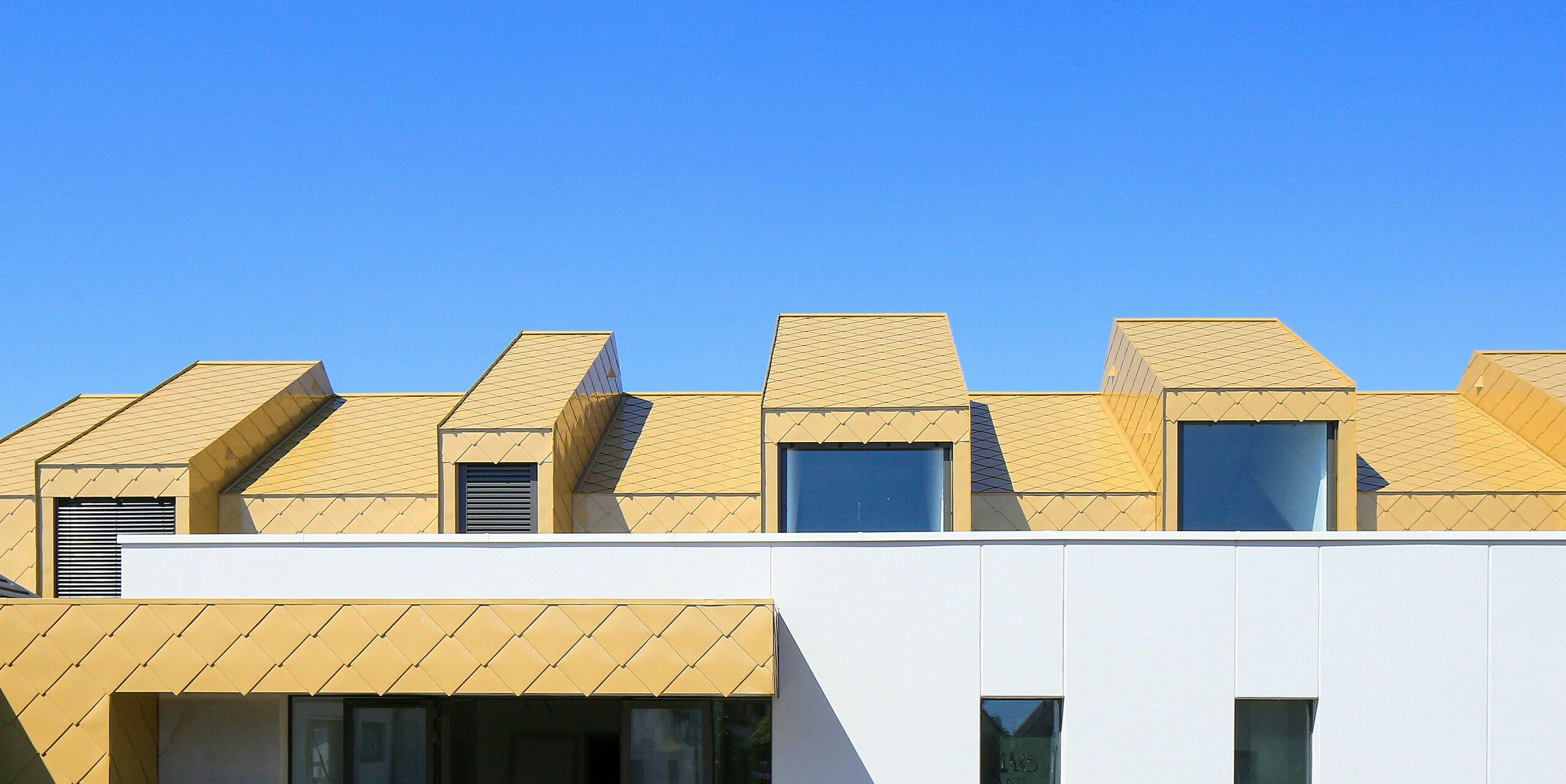 Dach und Fassade der obersten Etage am Gemeinde- und Kulturzentrum Fessenheim, Frankreich, wurden mit PREFA Dach- und Wandrauten 44 × 44 in Sparkling Gold eingedeckt.