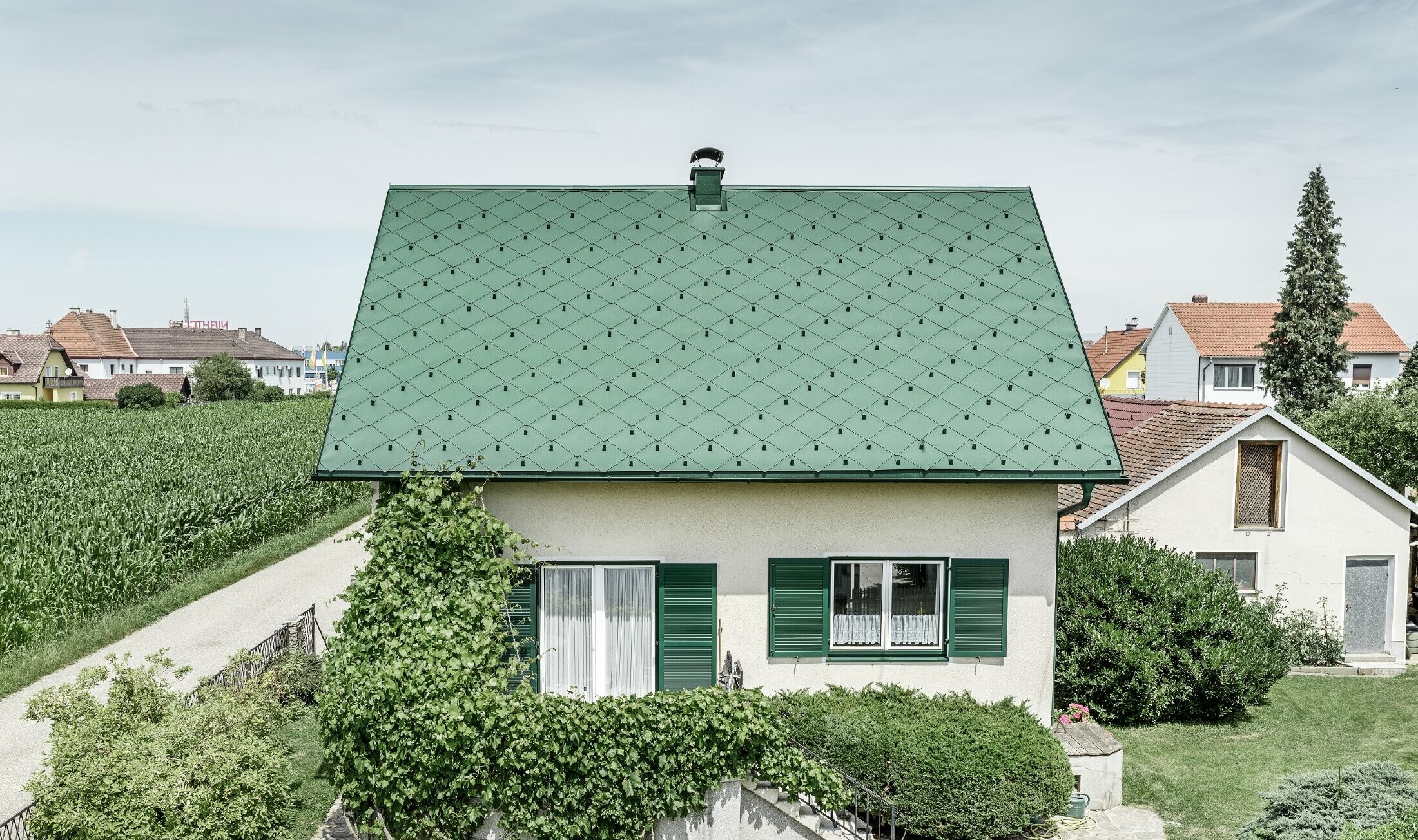 Toit à pignon de maison individuelle classique avec couverture en aluminium vert mousse et volets verts Le toit est recouvert de losanges de toiture PREFA 44 × 44 en P.10 vert mousse.