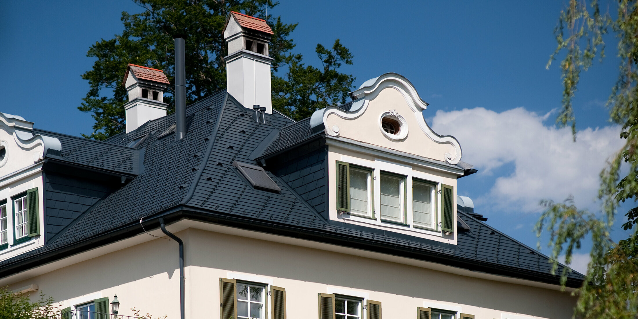 Nahaufnahme des Daches einer Villa in Bad Aussee, Österreich. Das Dach der Villa mit den prunkvollen Gauben wurde mit vielseitigen PREFA Dachschindeln in der Farbe P.10 Anthrazit eingedeckt.