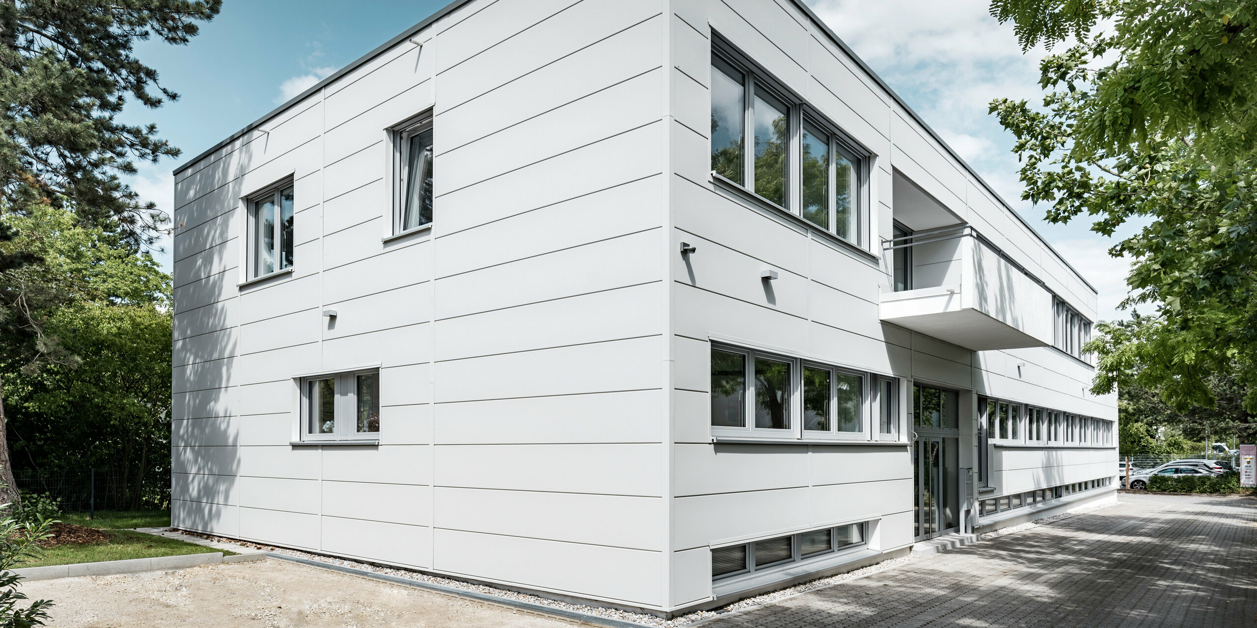 Des Sidings PREFA grand format entourent un bâtiment d'entreprise à Oberschleißheim (Allemagne). Les éléments de façade extra-larges en aluminium ont été choisis dans la couleur blanc Prefa.