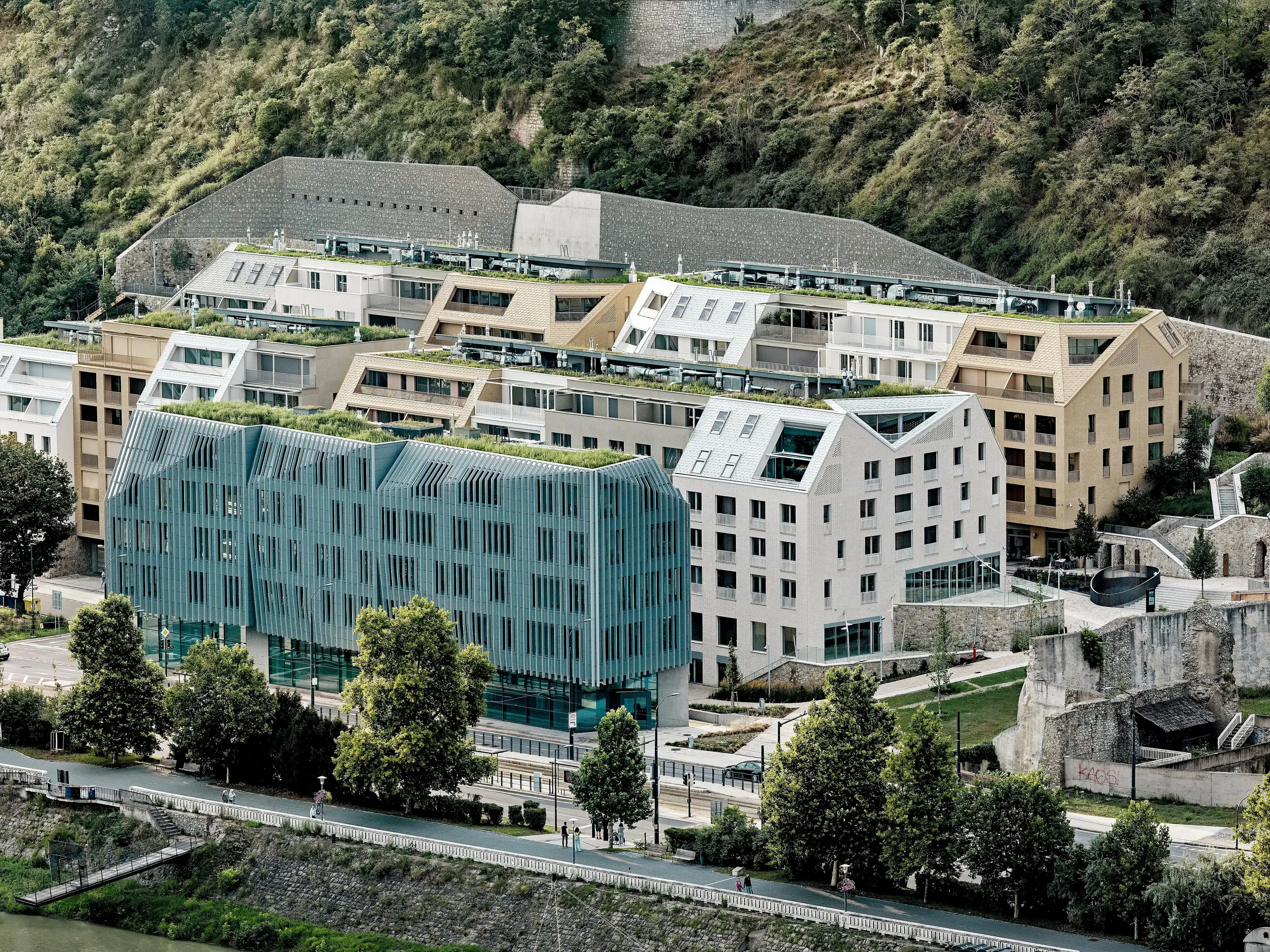 Beeindruckendes Gesamtbild des Stadtquartiers Vydrica in Bratislava am Donauufer: Die terrassierte Architektur mit begrünten Dachflächen, markanten Satteldächern und klaren Linien wird von PREFA Aluminium Dachschindeln in Prefaweiß, Sandbraun und Bronze geprägt. Die abwechslungsreiche Dachlandschaft mit integrierten Dachfenstern und präzisen Details zieht den Blick über das gesamte Ensemble. PREFA Aluminium ermöglicht filigrane, komplexe Formen und überzeugt durch Langlebigkeit, geringes Gewicht und extreme Witterungsbeständigkeit – ideal für nachhaltige, architektonisch anspruchsvolle Stadtprojekte.