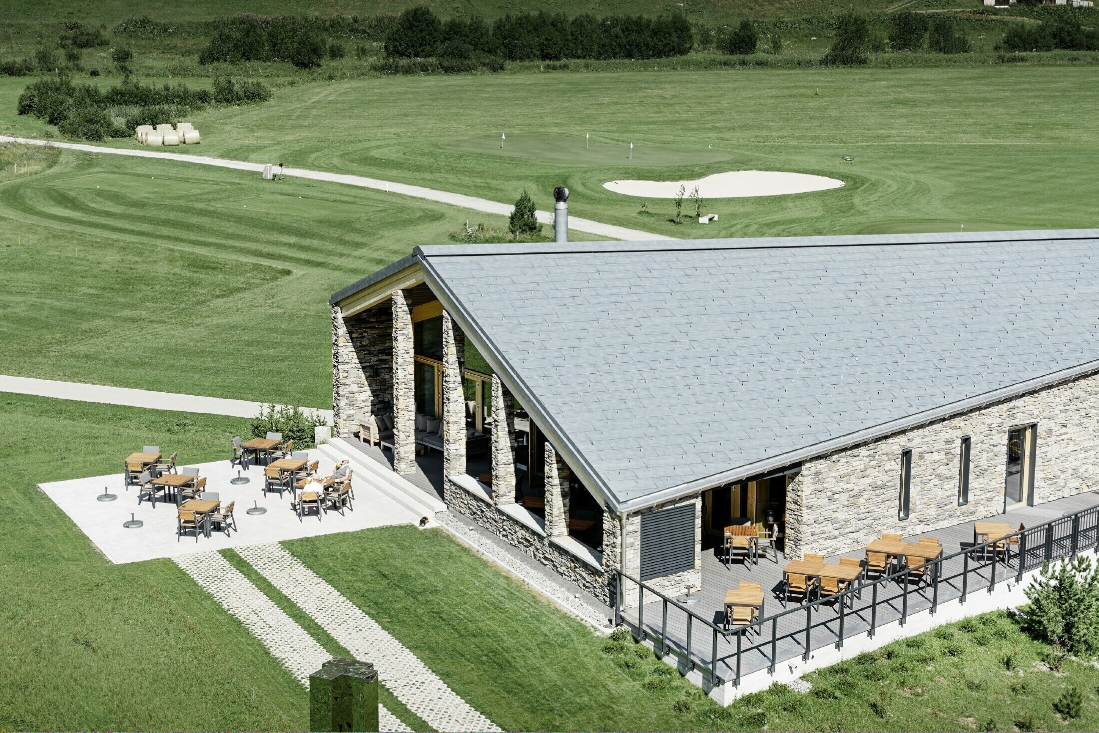 Club-house moderne du parcours de golf d’Andermatt en Suisse — Façade en pierre et panneaux de toiture FX.12 PREFA en aluminium de couleur gris pierre