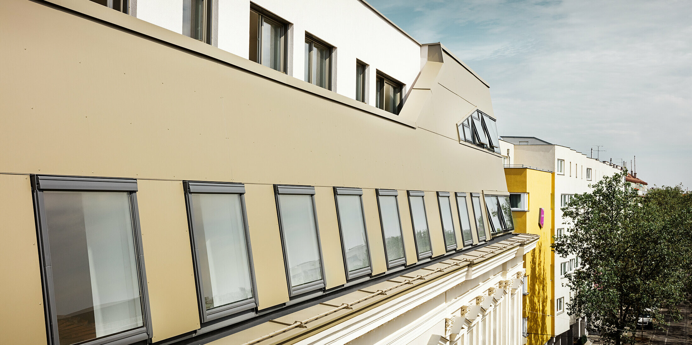 Die seitliche Ansicht des Dachgeschosses hebt die gleichmäßige Verkleidung mit PREFA Aluminium Verbundplatten in Bronze hervor. Große Fenster und flächige Glaselemente sorgen für lichtdurchflutete Räume und ein elegantes, modernes Erscheinungsbild.