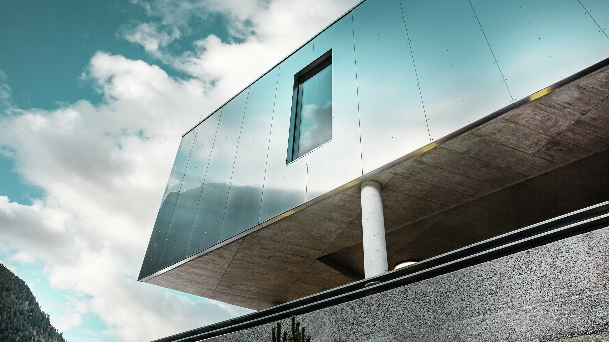 Architecture moderne du supermarché MPREIS à Sölden, au Tyrol, avec des panneaux composites en aluminium PREFA réfléchissants dans la couleur spéciale Reflective Natural. La façade brillante reflète le ciel et le paysage montagneux. Des lignes épurées et des colonnes massives en béton allient un design innovant à la stabilité et à l'élégance.