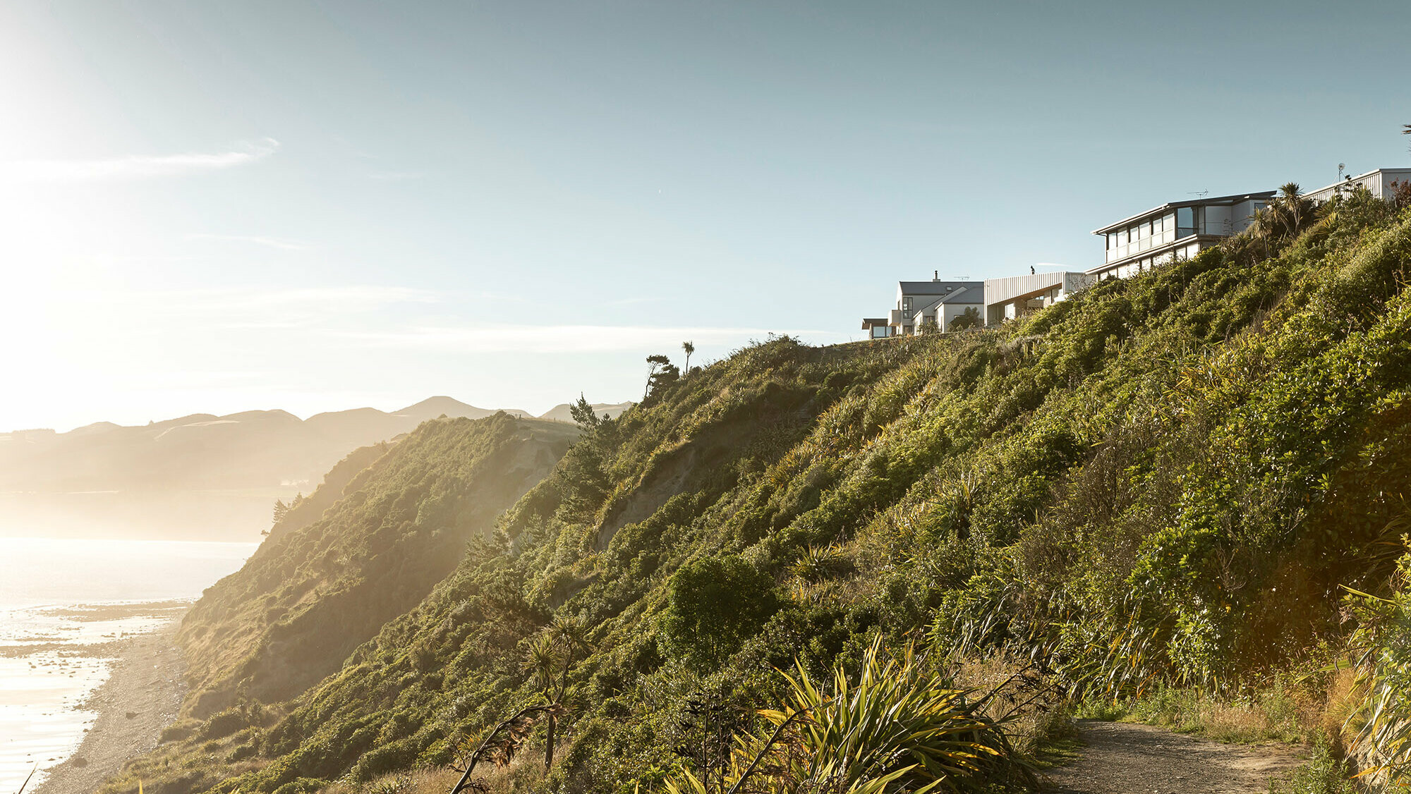 Aufnahme von der Landschaft Motunaus, darauf sichtbar der Strand von Motunau, die Vegetation sowie die Klippen, an deren Rand ein paar Häuser gebaut wurden, unter anderem auch das Whitecaps House von Three Sixty Architecture.