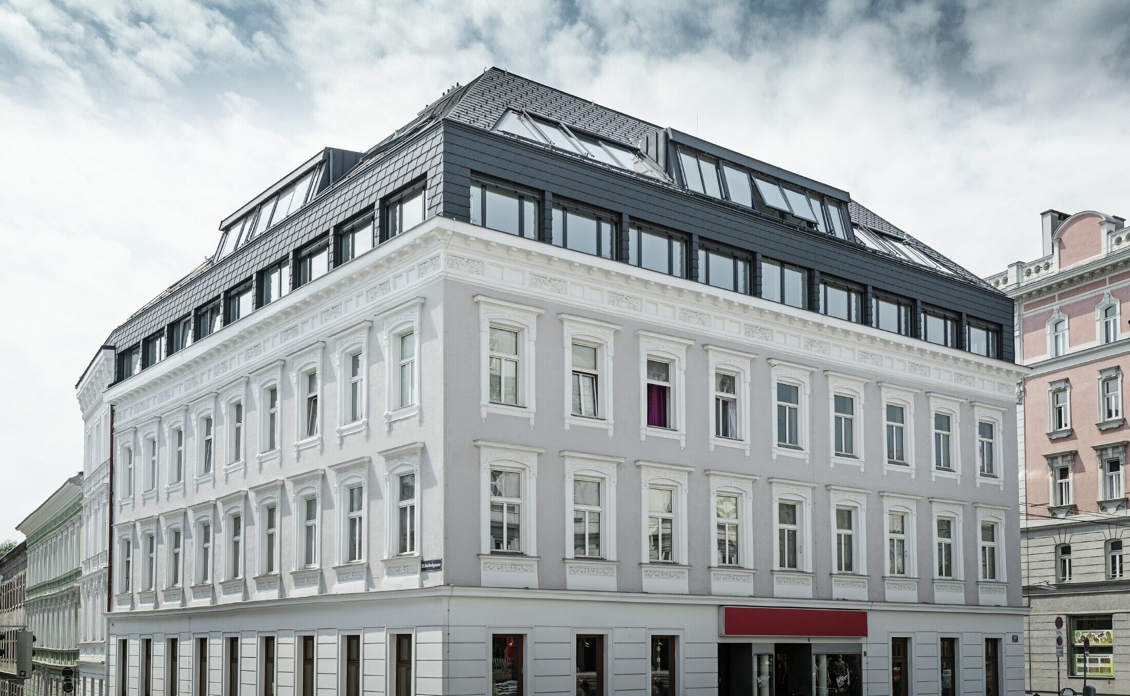 Straßenansicht eines Wohnhauses in der Mariahilferstraße in Wien. Das Dachgeschoß wurde ausgebaut und mit der PREFA Dachschindel und Wandschindel in Anthrazit verkleidet.