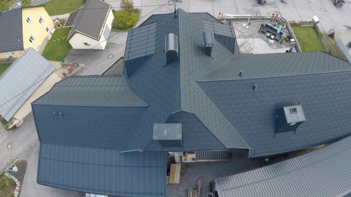 Dakrenovatie van een groot dakoppervlak met veel details - kimmen, koekkoeken en schoorstenen. Het dak is gedekt met de aluminium dakplaat R.16 van PREFA in antraciet.