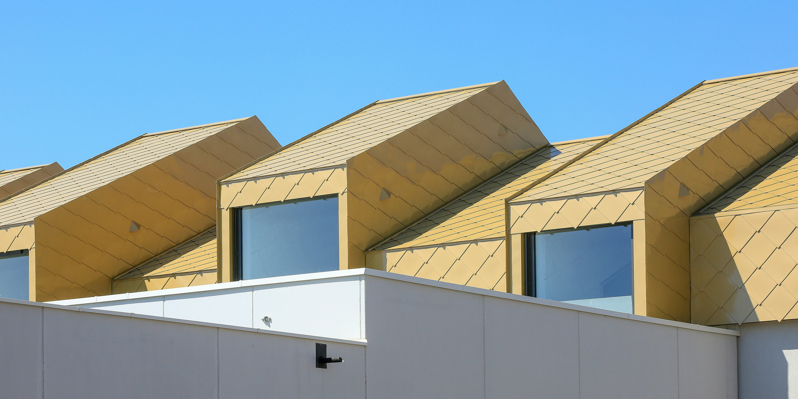 Blick von der Straße auf das Gemeinde- und Kulturzentrum Fessenheim (FRA). Die oberste Etage und das Dach des Gebäudes wurden mit PREFA Dach- und Wandrauten 44 × 44 in Sparkling Gold verkleidet.